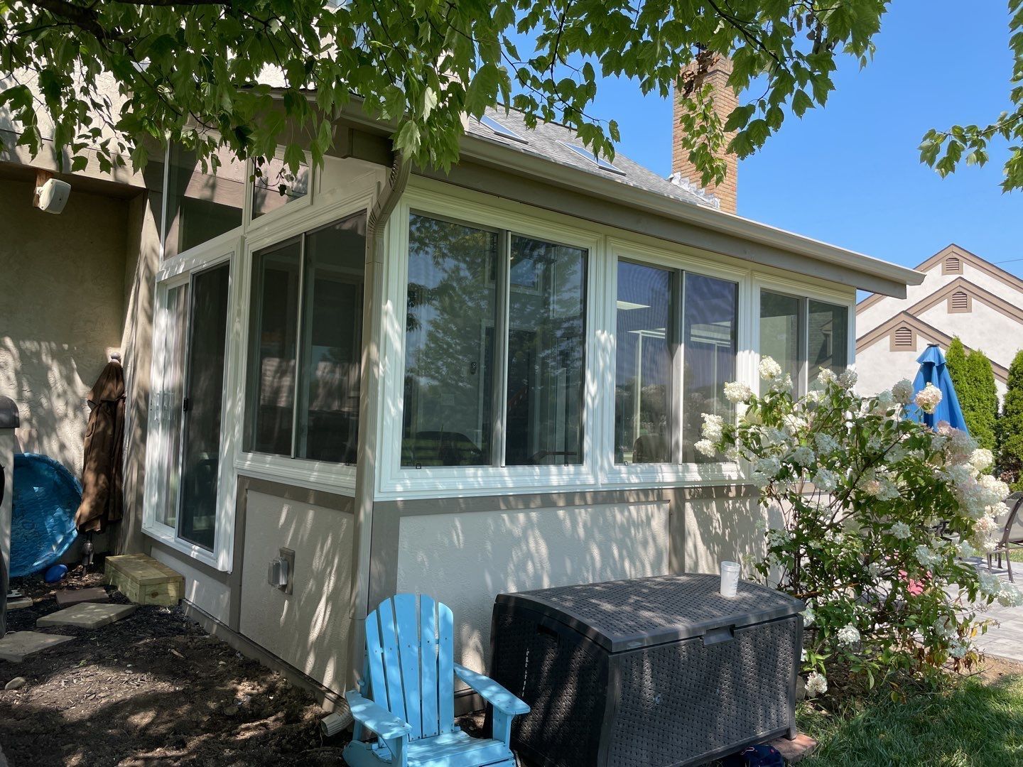 Backyard sunroom with white trim, large windows, blue chair, and covered table under a tree