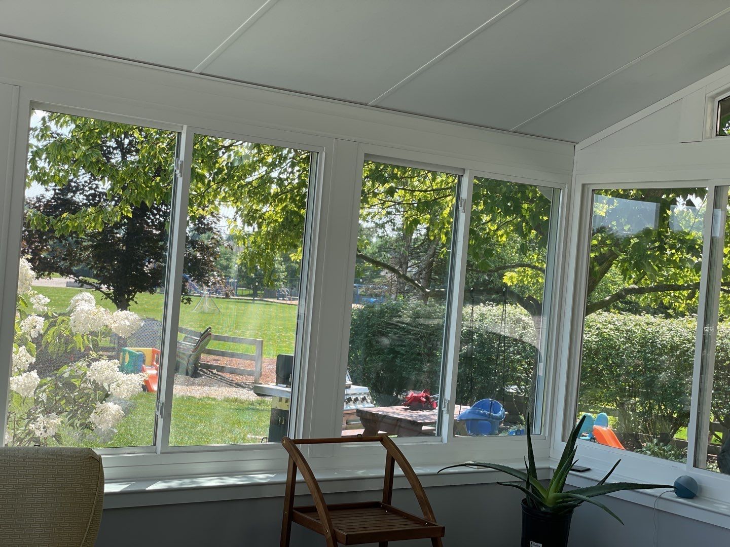 Sunroom with large windows overlooking a green yard, chair in front, and potted plant by the corner.
