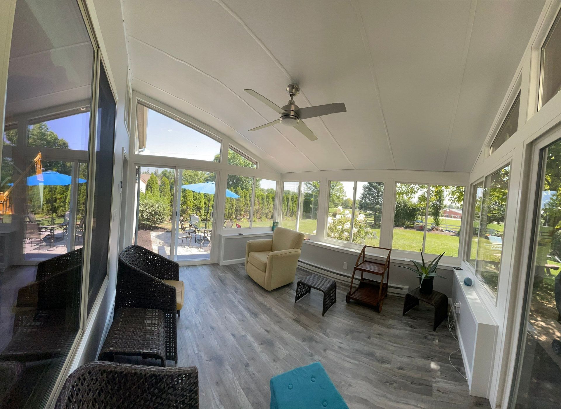 Screened porch with wicker chairs, ceiling fan, and view of a sunny yard