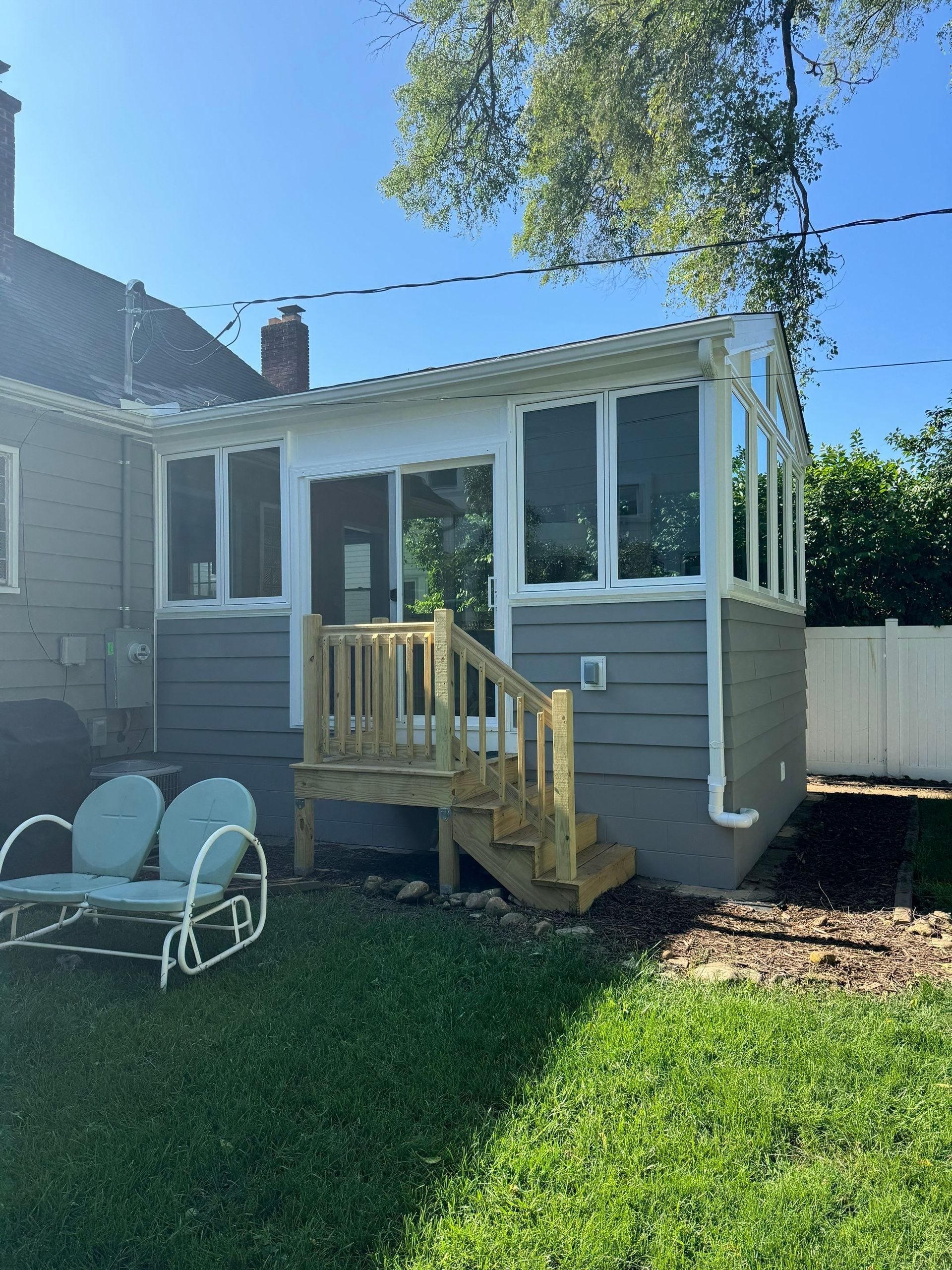 Backyard house addition with gray siding, white trim, and small wooden steps under a sunny sky