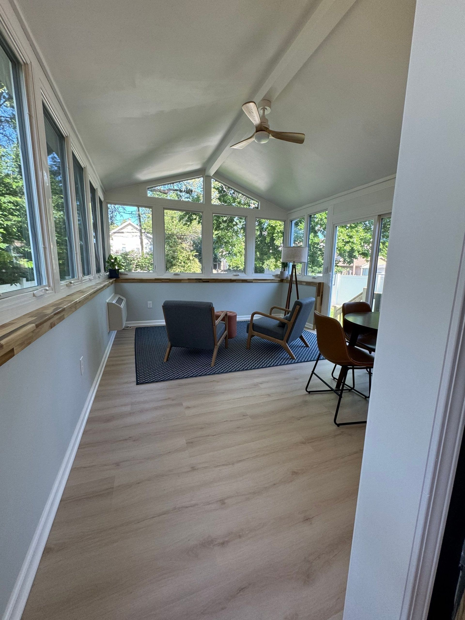 Sunroom with light wood floors, large windows, a ceiling fan, and patio chairs around a rug