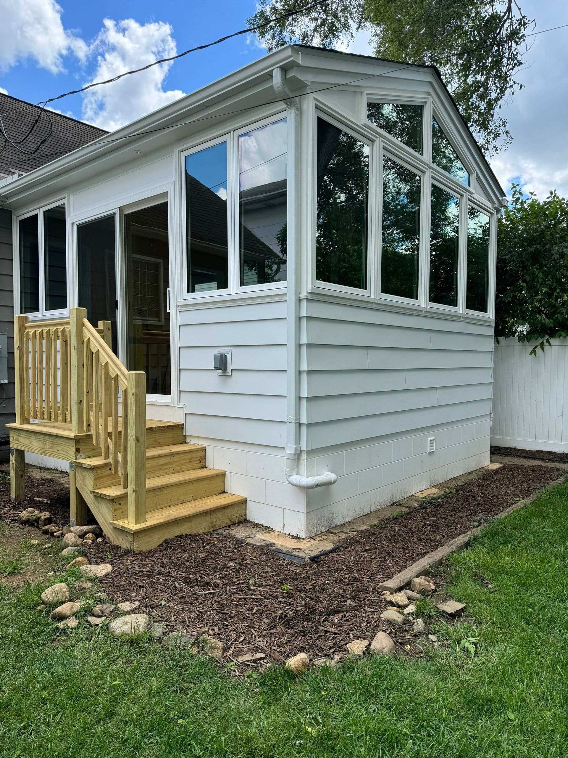 White sunroom addition on a house with screened windows and a small wooden stair ramp on the side.