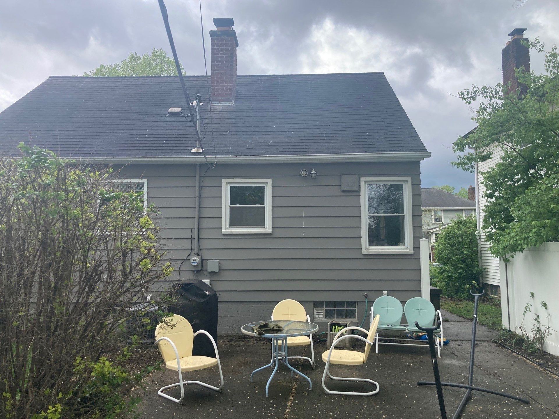 Backyard patio with pastel chairs, small table, and a gray house in the background