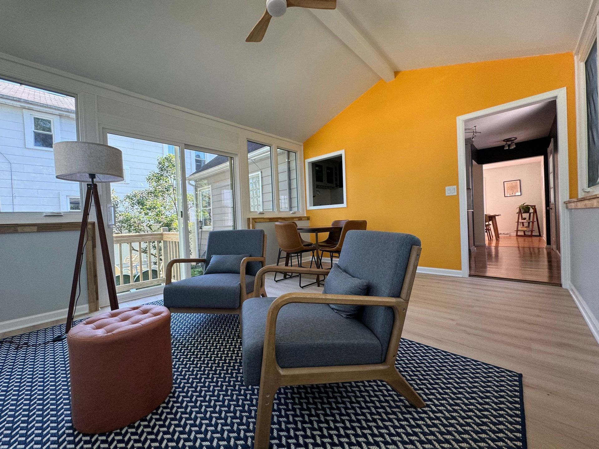 Bright living room with blue chairs, yellow accent wall, rug, and view of a screened porch.