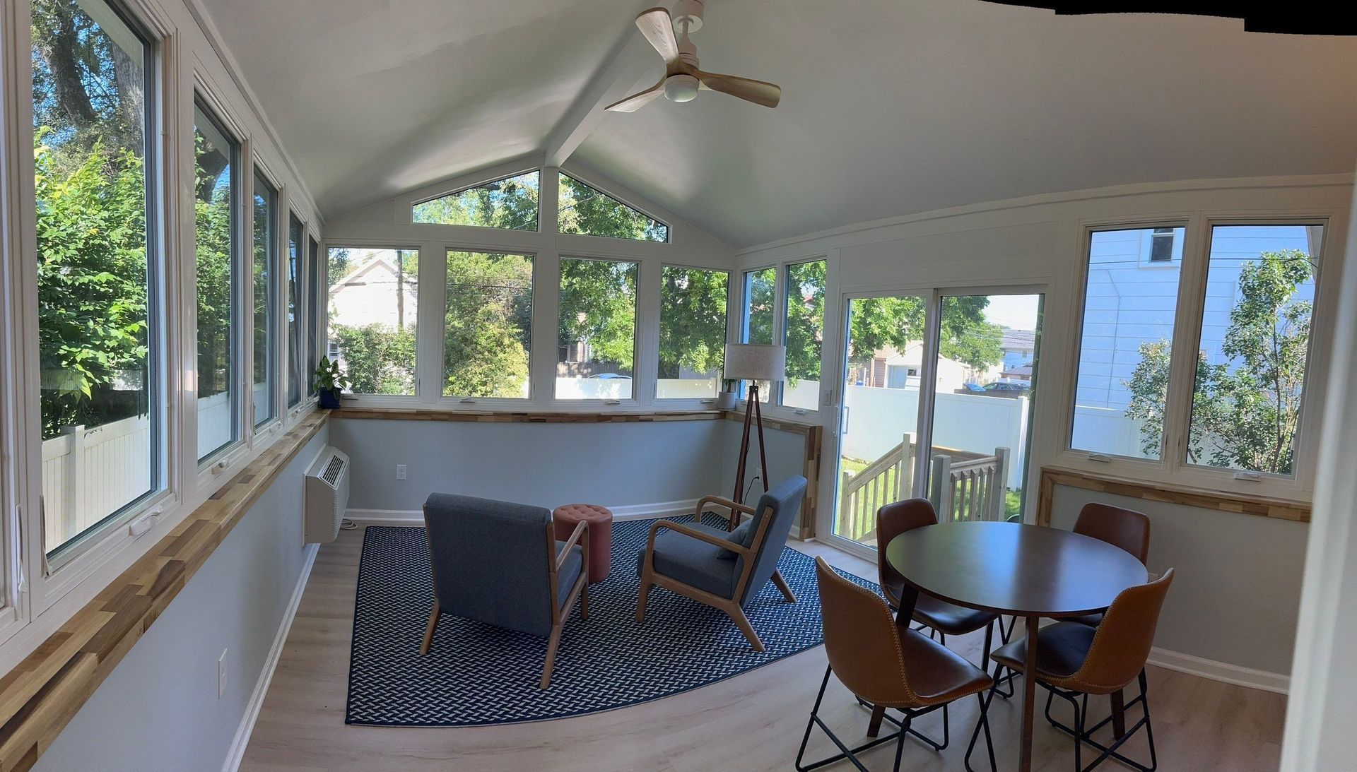 Bright sunroom with windows, ceiling fan, patterned rug, chairs, and small round dining table.