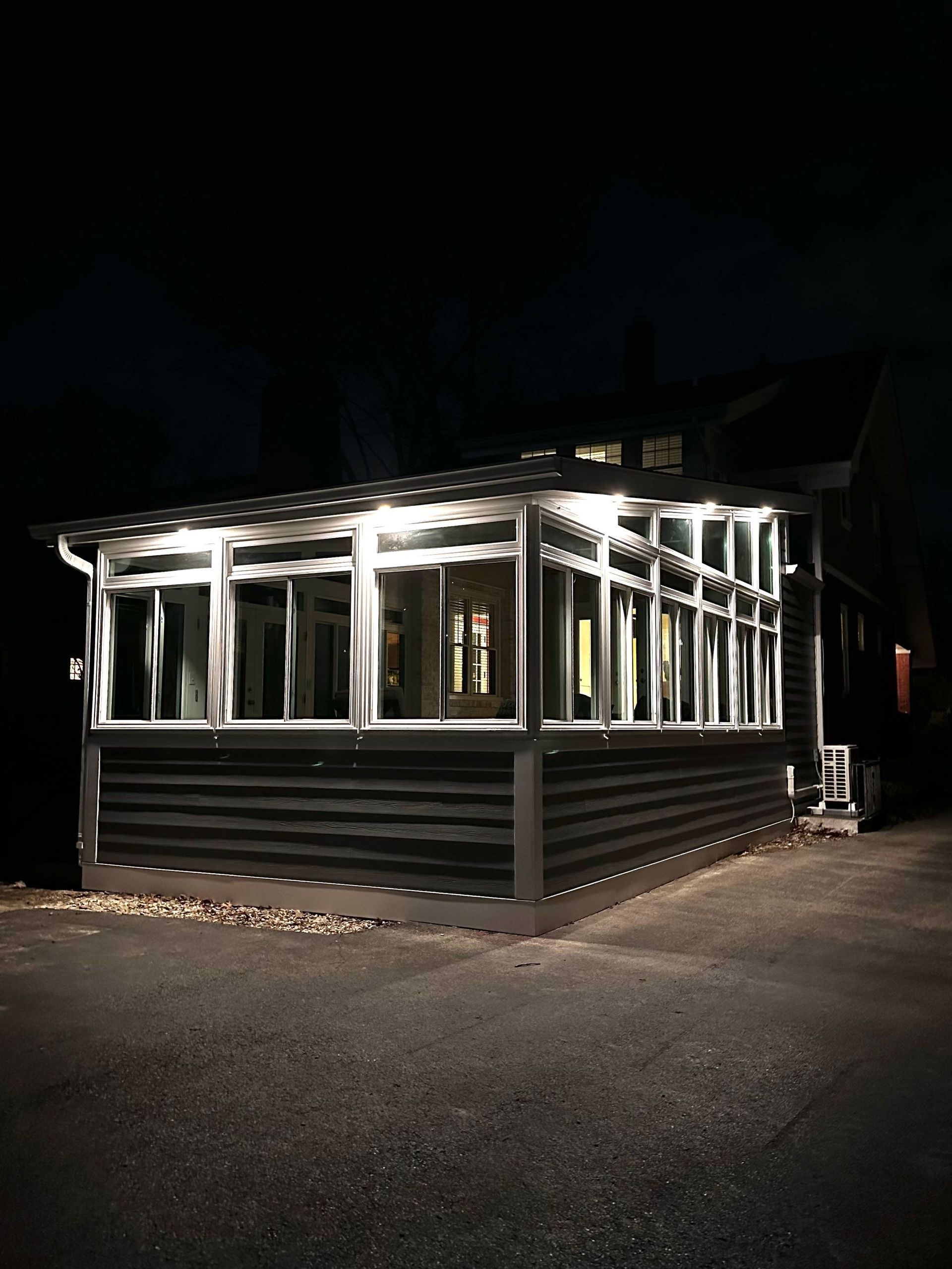 Lit-up glass-walled building at night with black siding and illuminated windows