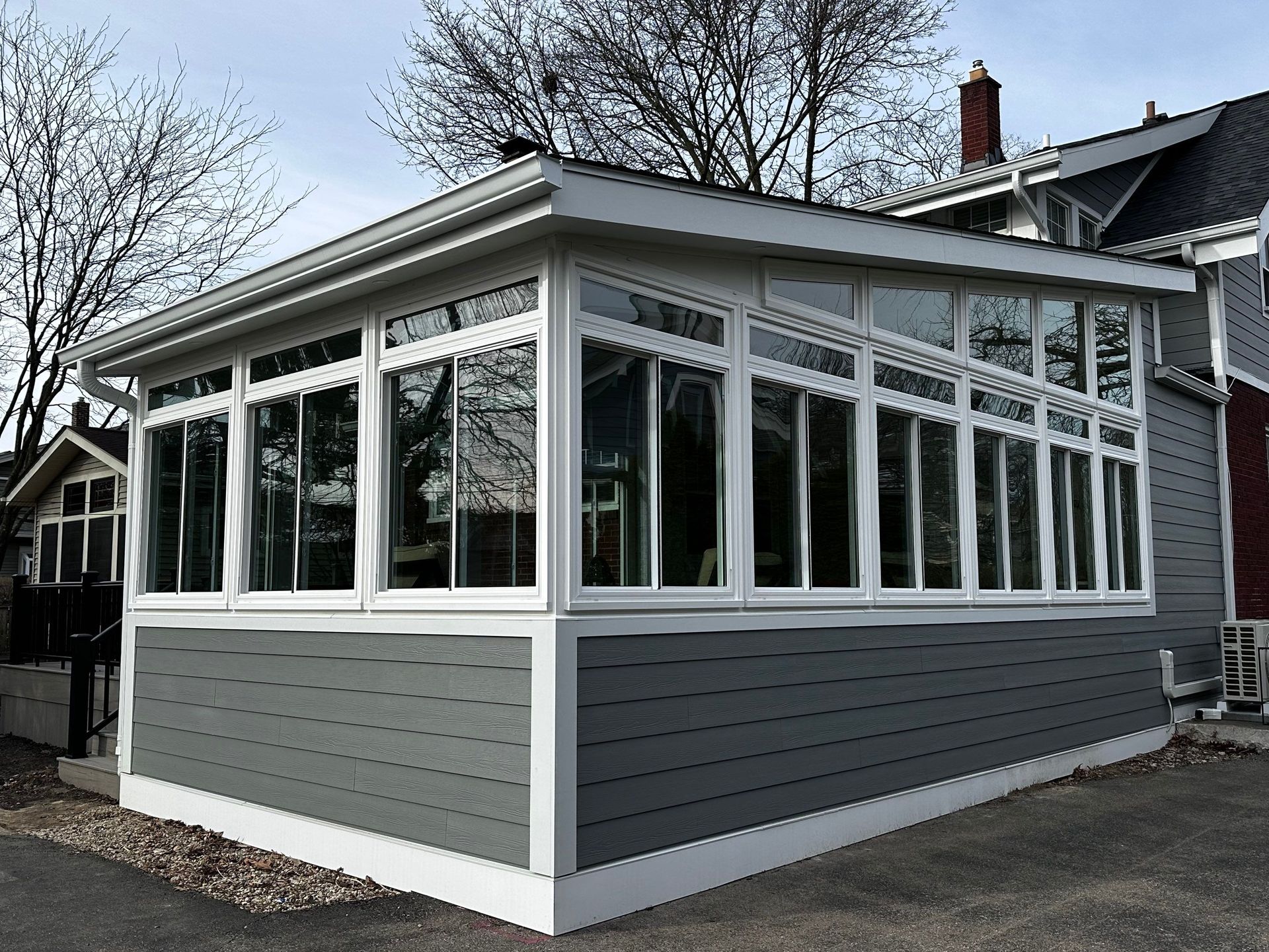 White and gray sunroom addition on a house with large windows and a sloped roof