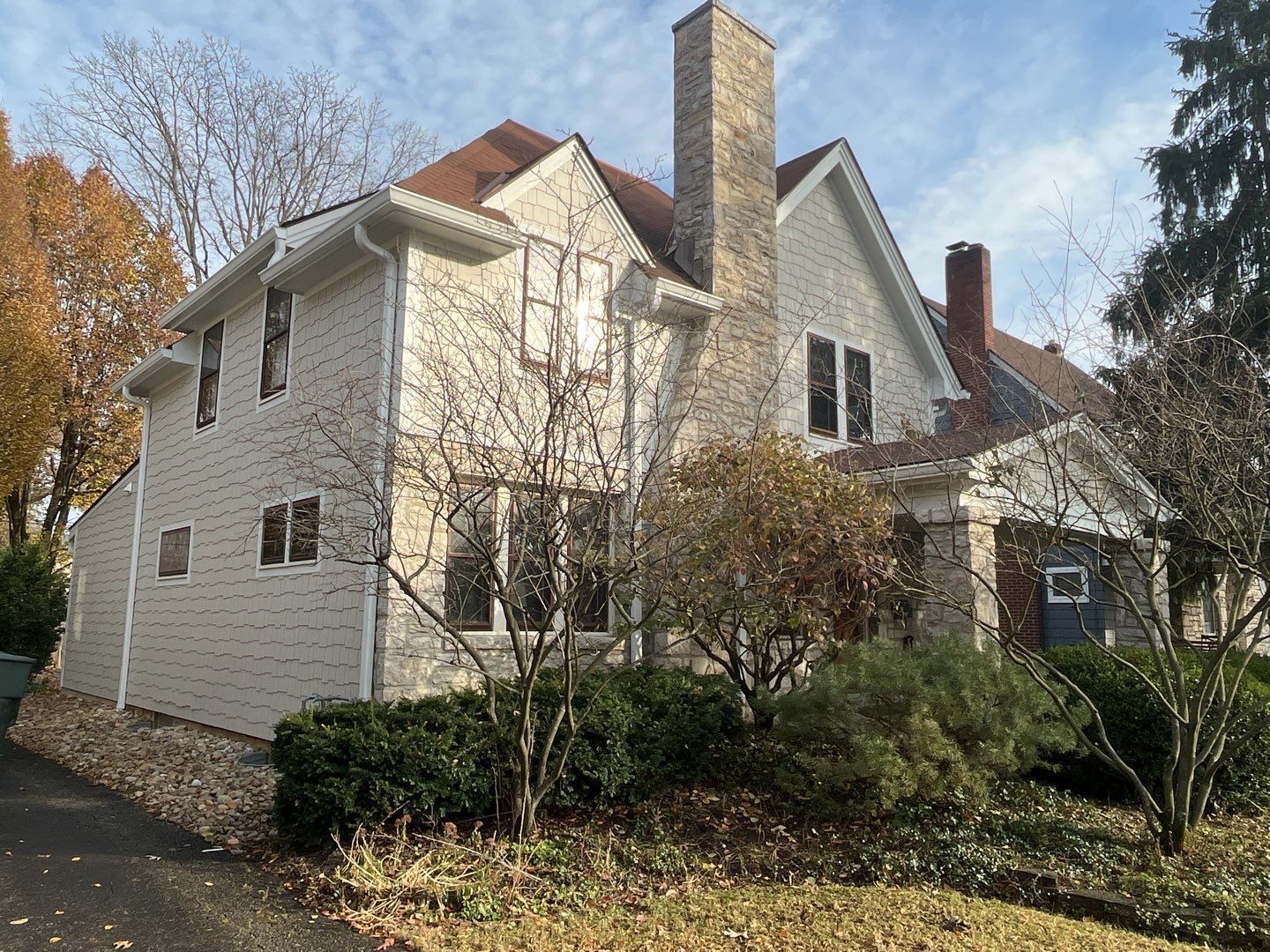 White house with chimney and gabled roof, surrounded by trees and shrubs in autumn.