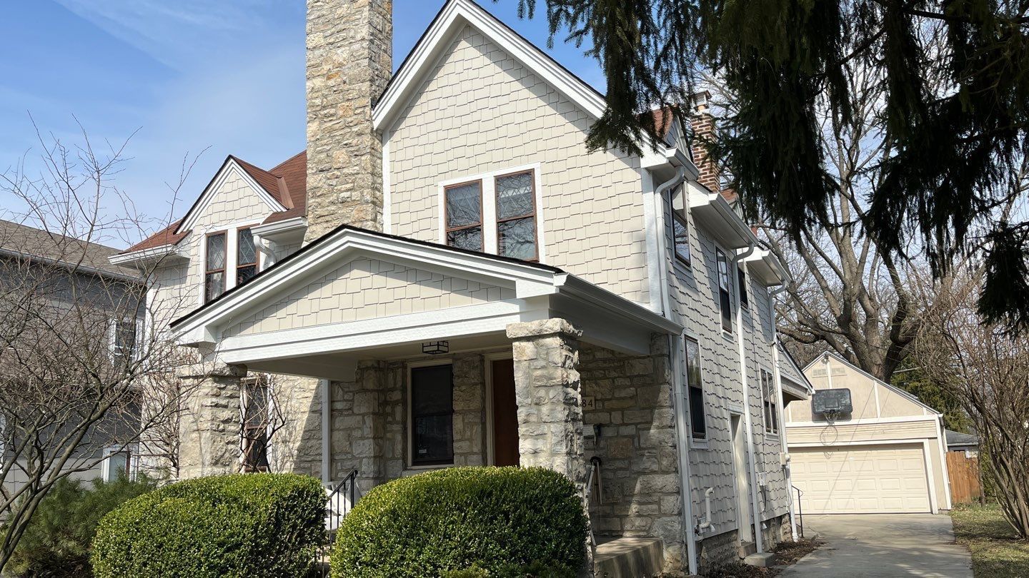 Stone house with white trim and front porch, viewed from the driveway on a sunny day