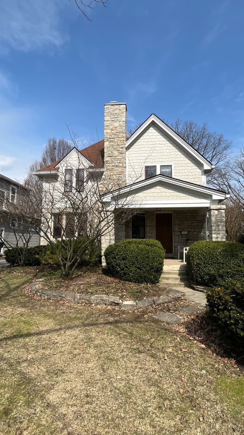Suburban house with stone chimney, front porch, and leaf-strewn yard under a blue sky