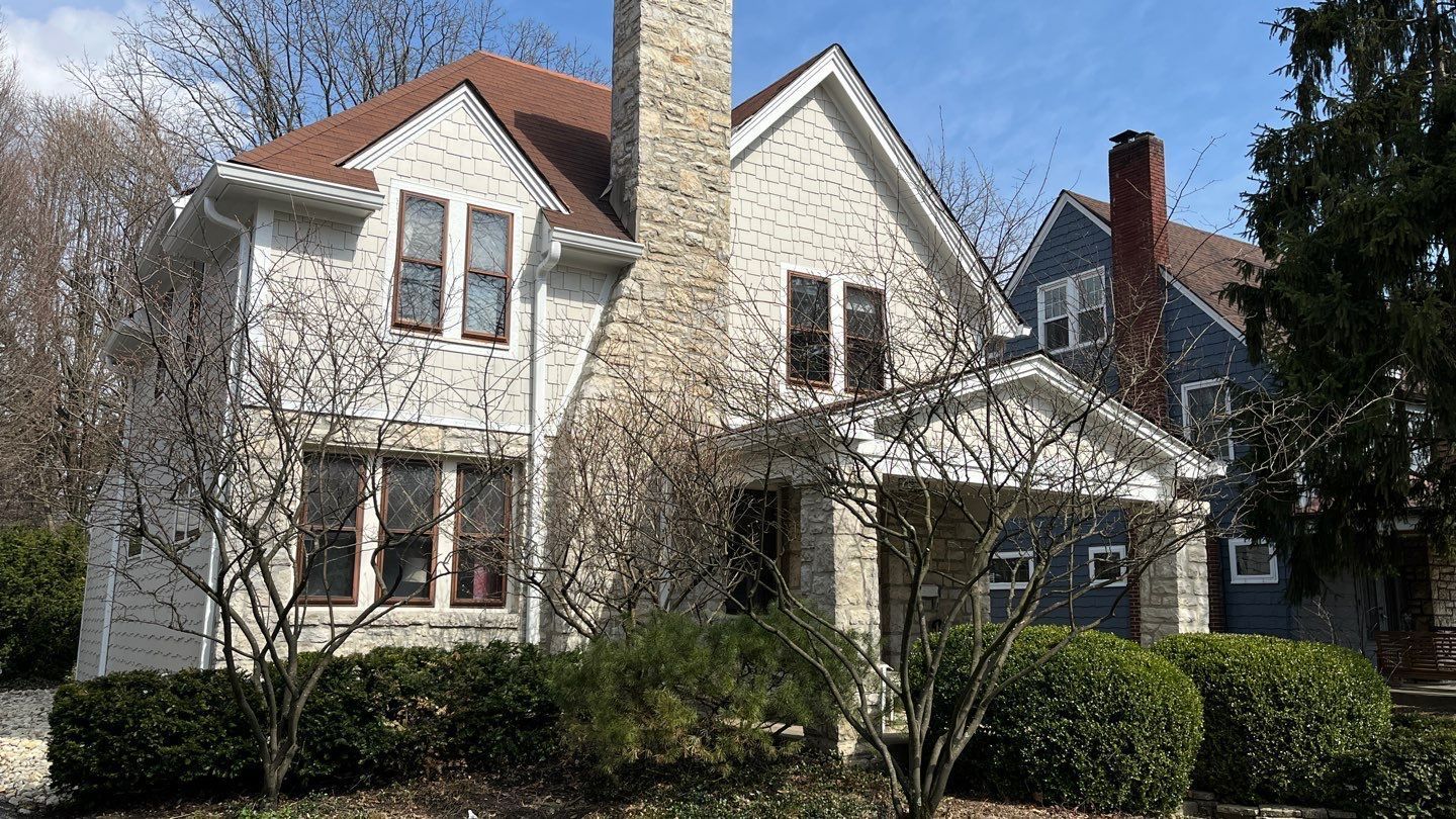 White two-story house with steep gables, front porch, and shrubs under a blue sky