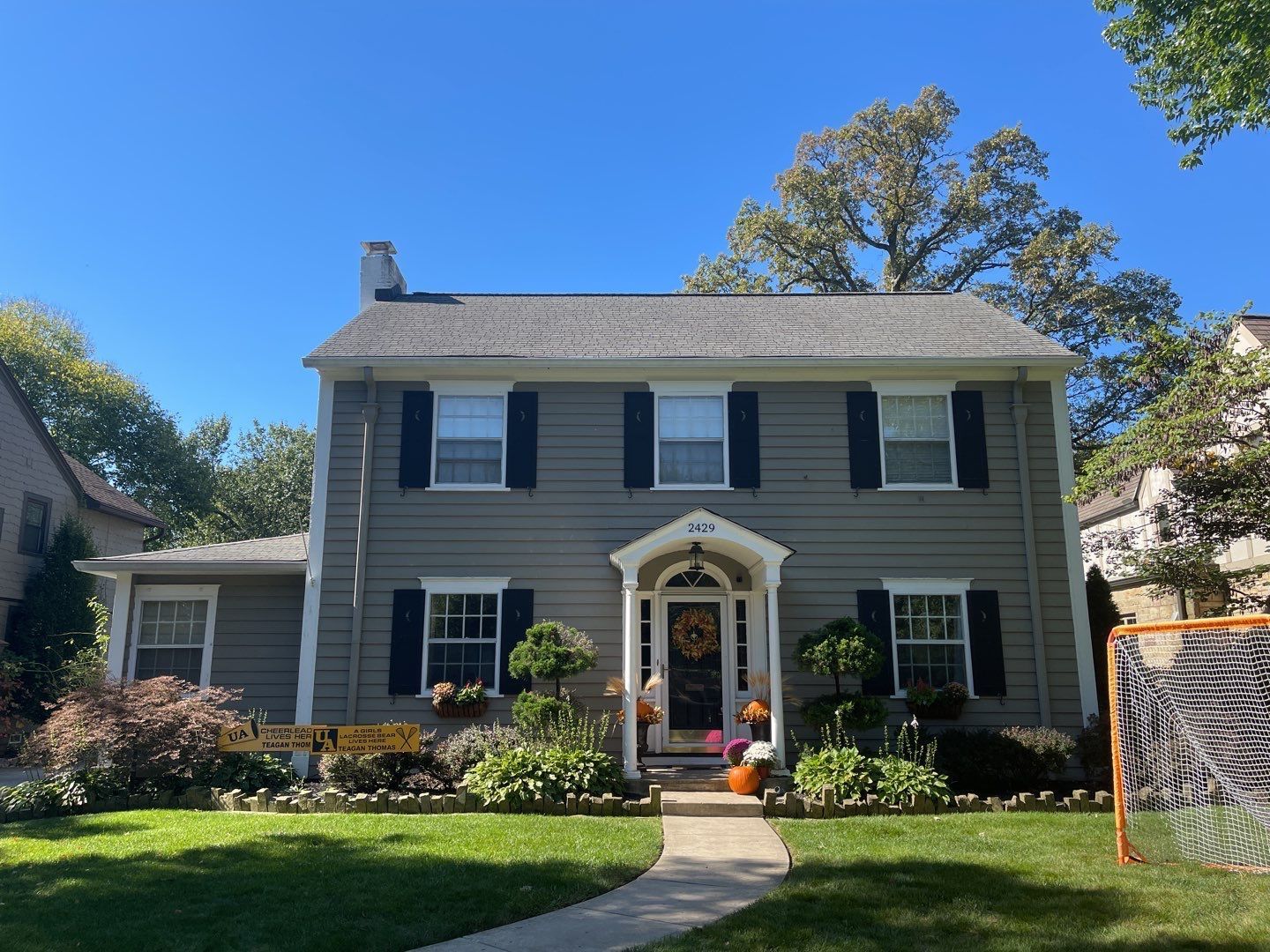 Gray two-story house with black shutters, white trim, and a front garden under a blue sky