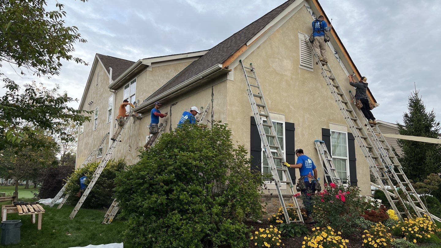 Workers on ladders painting the exterior of a beige house with flowers in front.