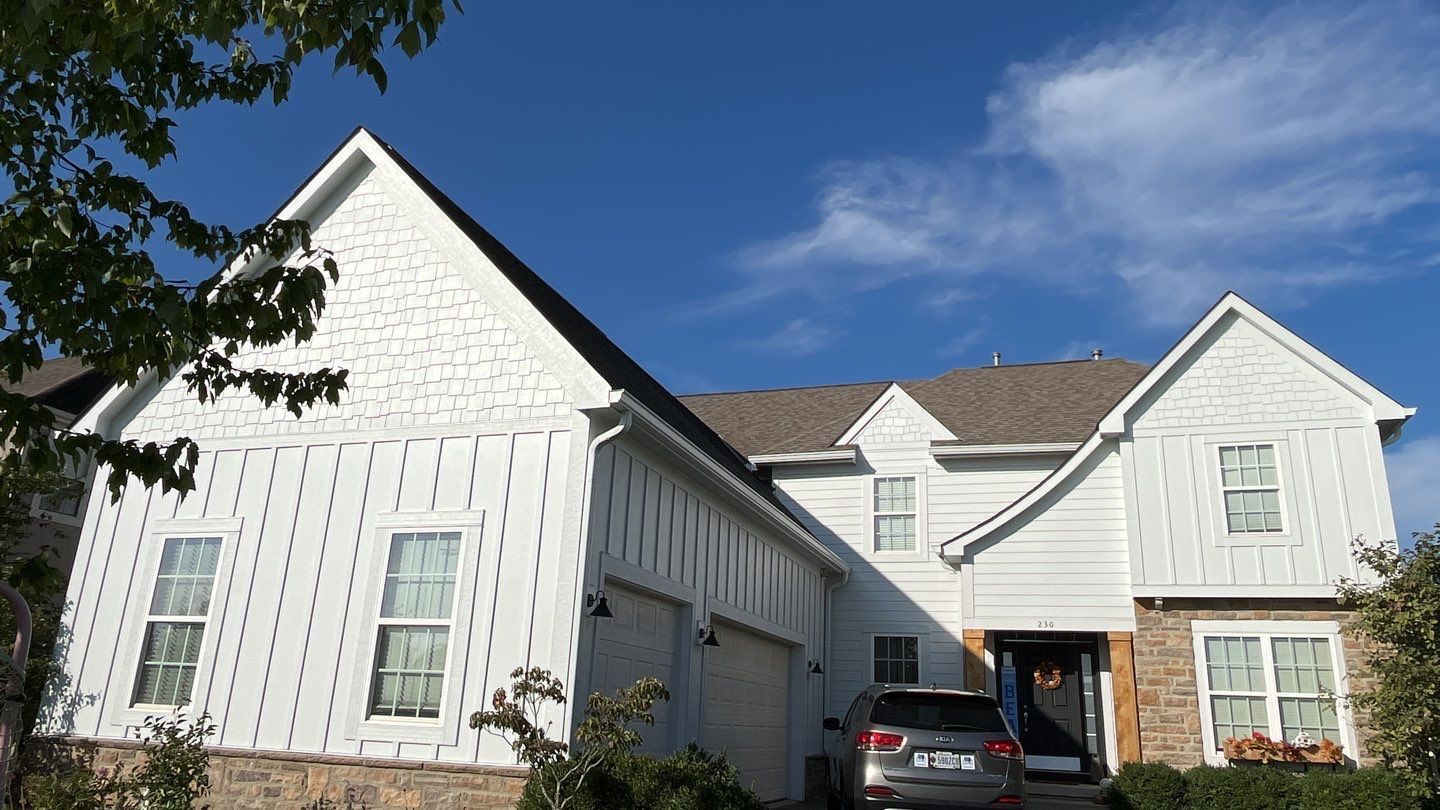 White two-story suburban house with dark roof, front driveway, and parked black car under a blue sky