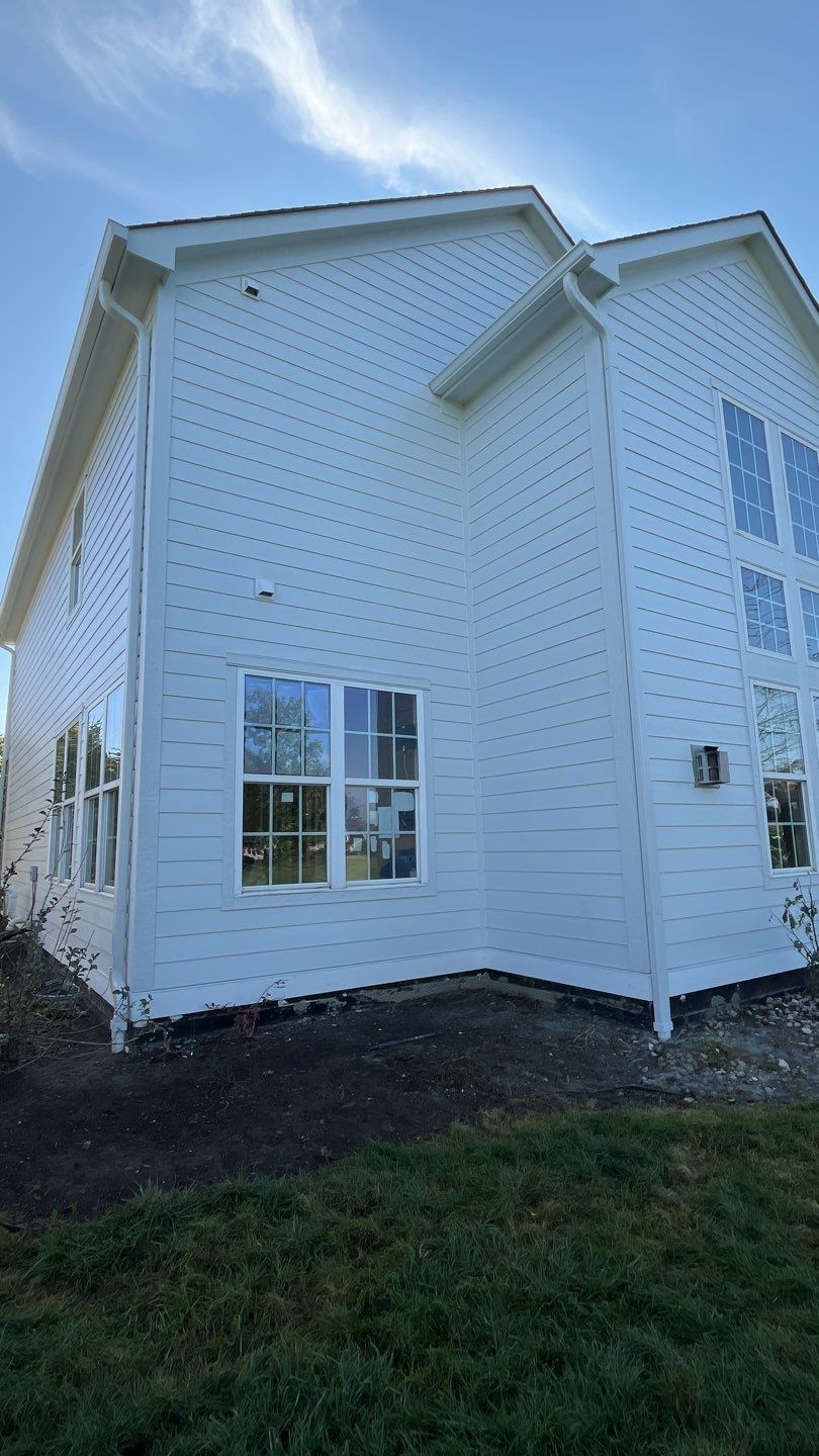 White two-story house exterior with blue sky, white siding, windows, and dark mulch along the foundation