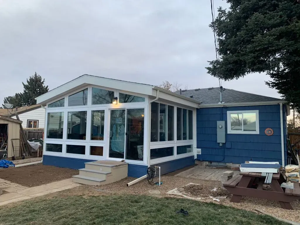 Blue house addition with large windows and a small porch in a suburban yard