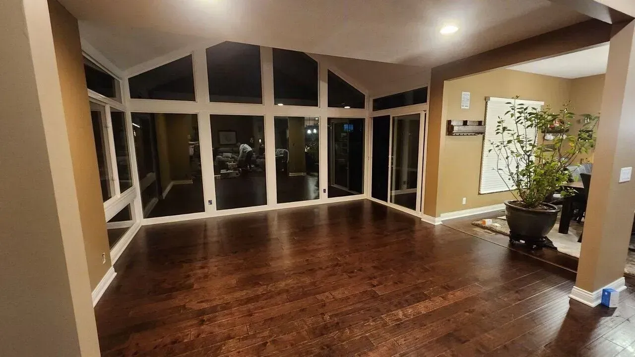 Empty living room with dark wood floors, large windows, and a plant in the corner at night