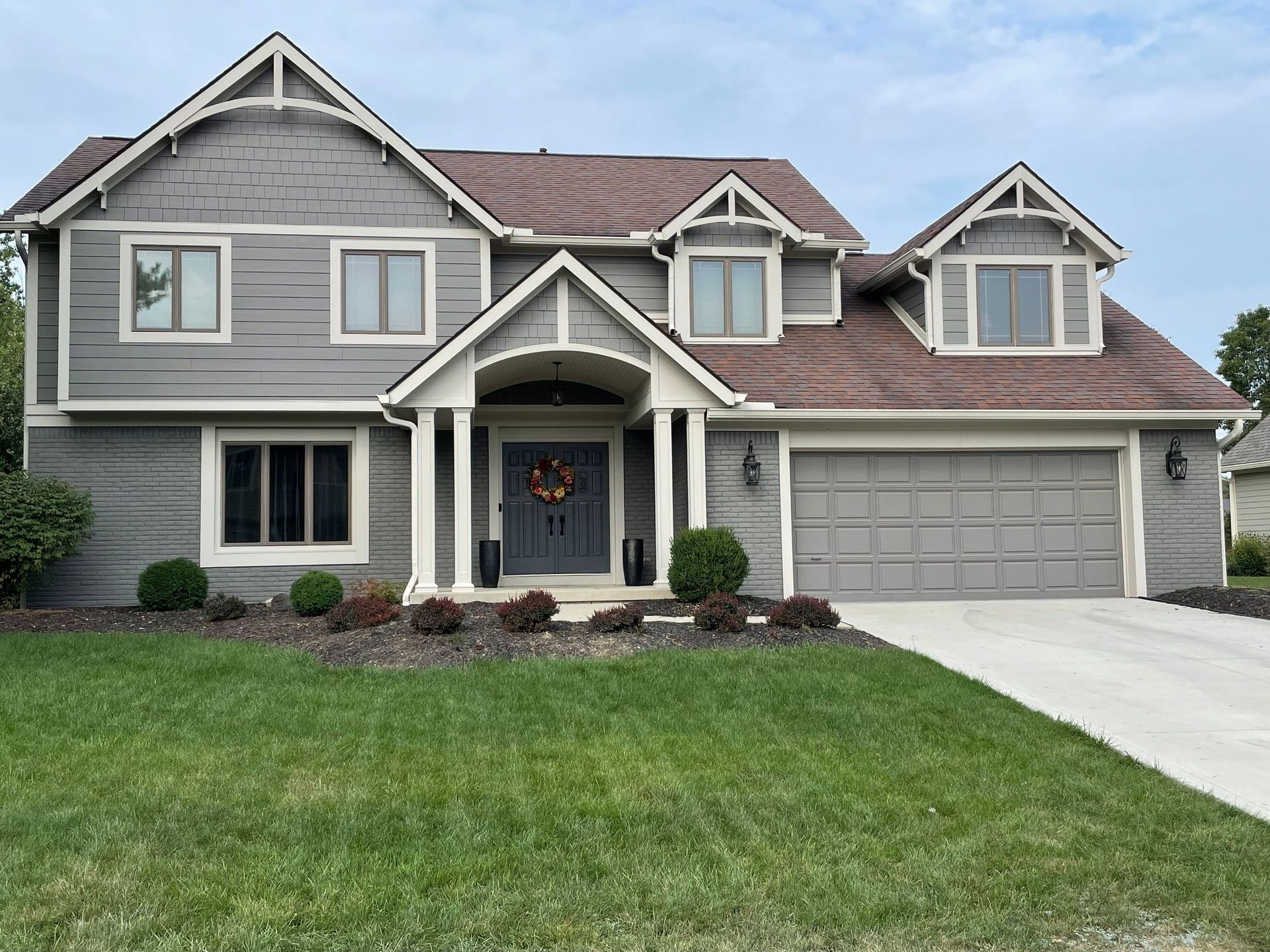 Gray suburban house with white trim, gabled roof, two-car garage, and a green front lawn