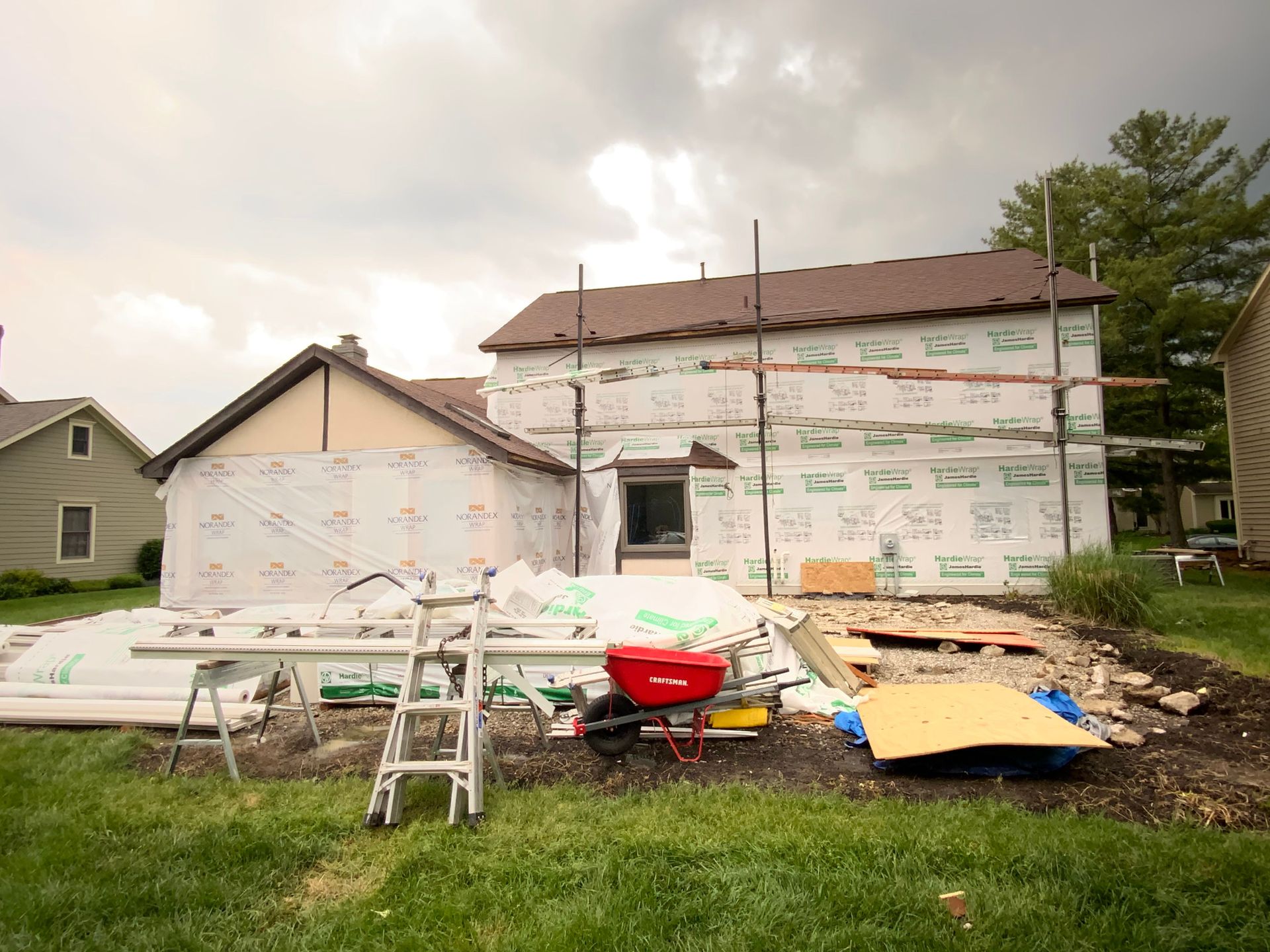 House under renovation with new siding, ladder, wheelbarrow, and construction debris in front yard