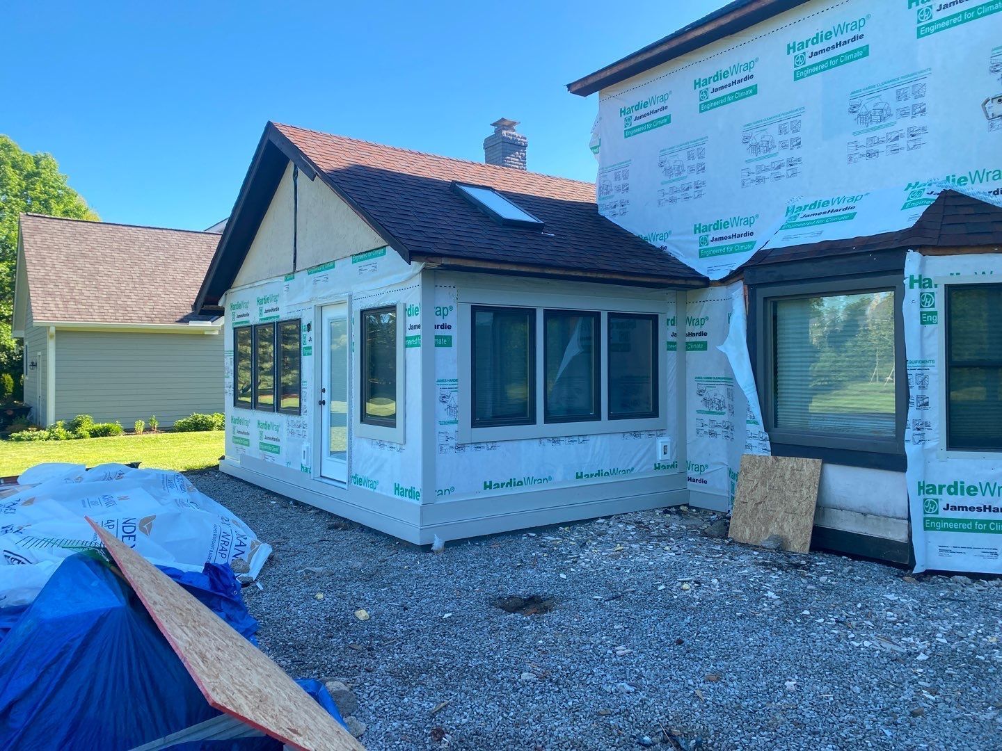 Partially built house with white siding, roof shingles, and construction wrap on a gravel lot