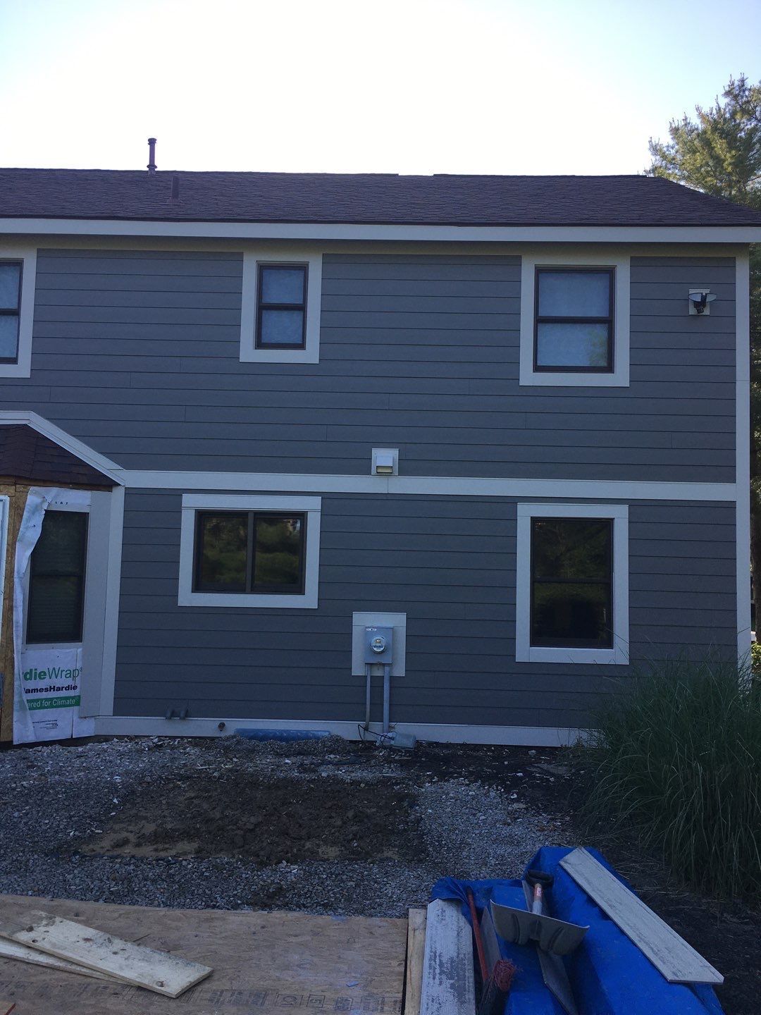 Gray two-story house exterior with white trim and a gravel yard under a bright sky