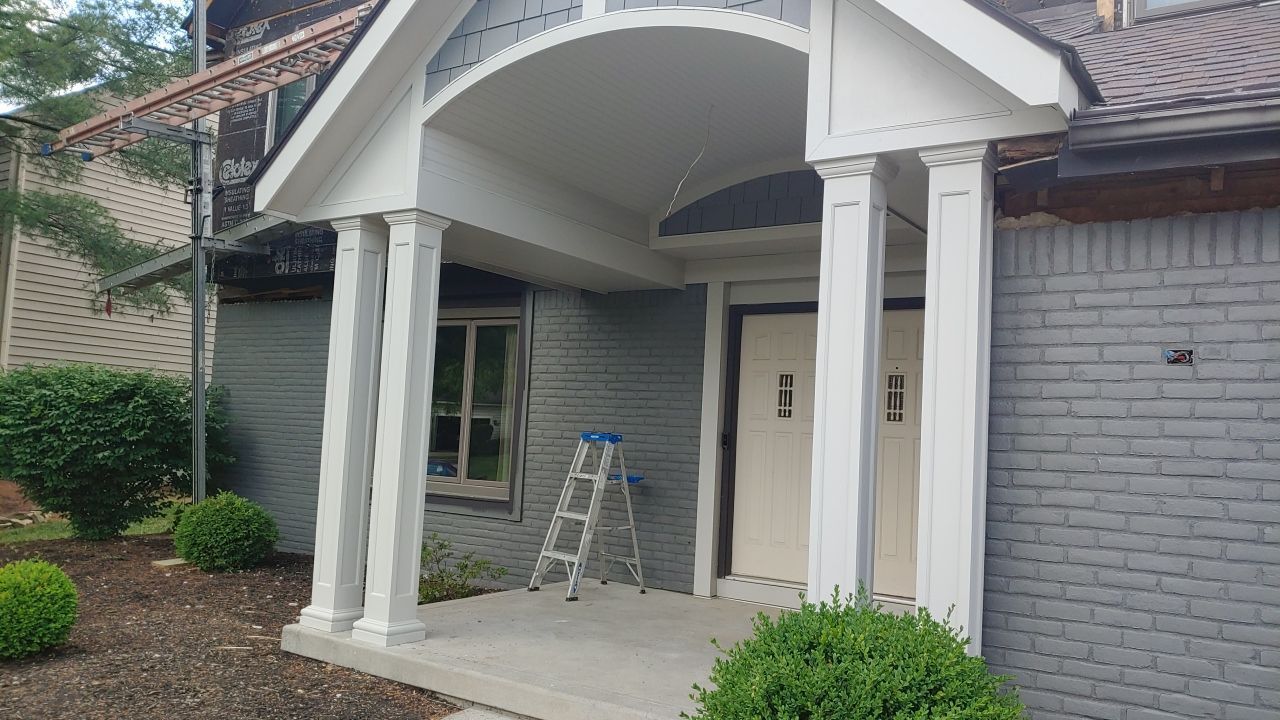 Front entrance of a house with a small porch, white columns, and a ladder near the doorway.