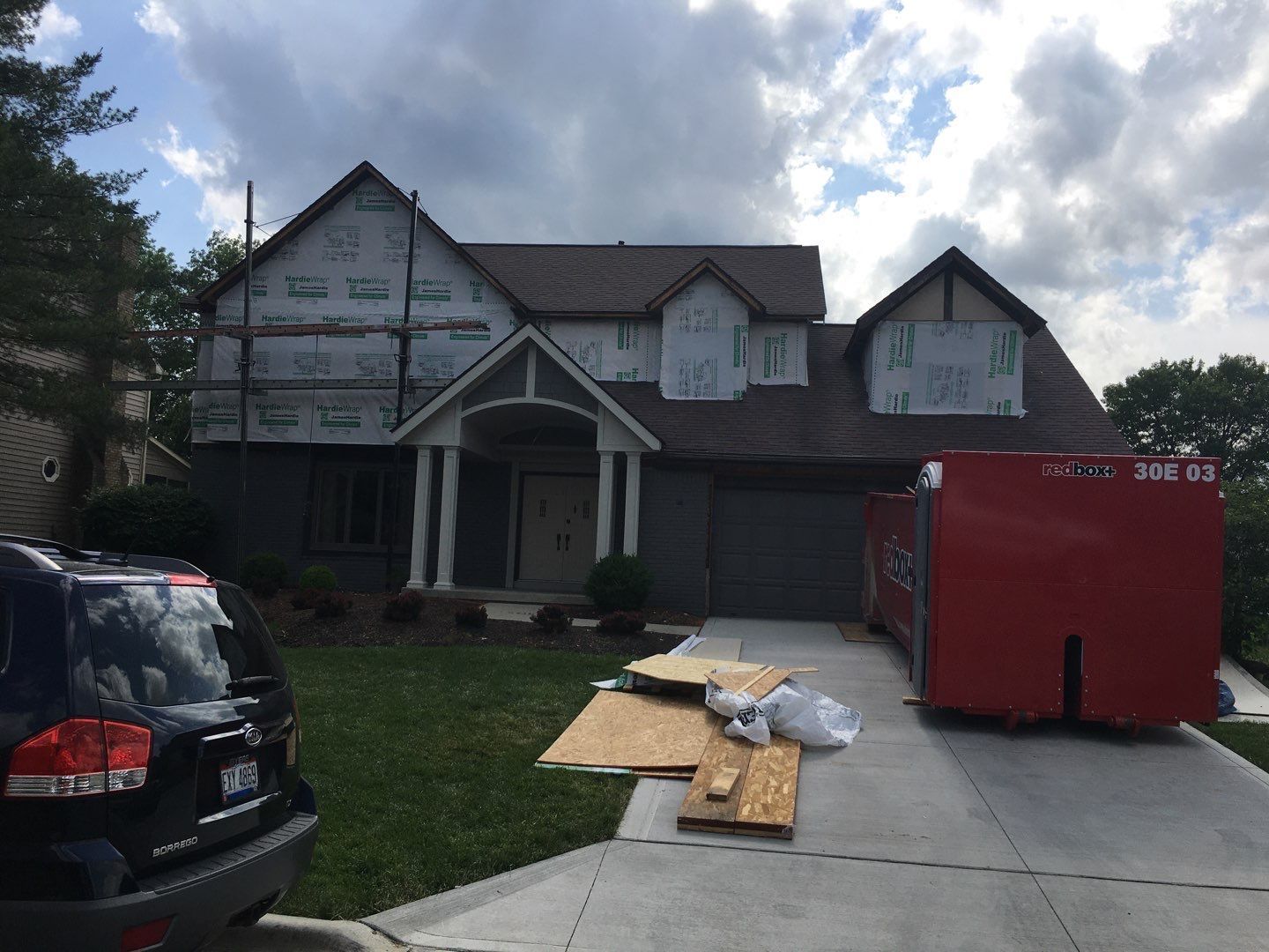 House under construction with red dumpster, parked car, and materials on driveway