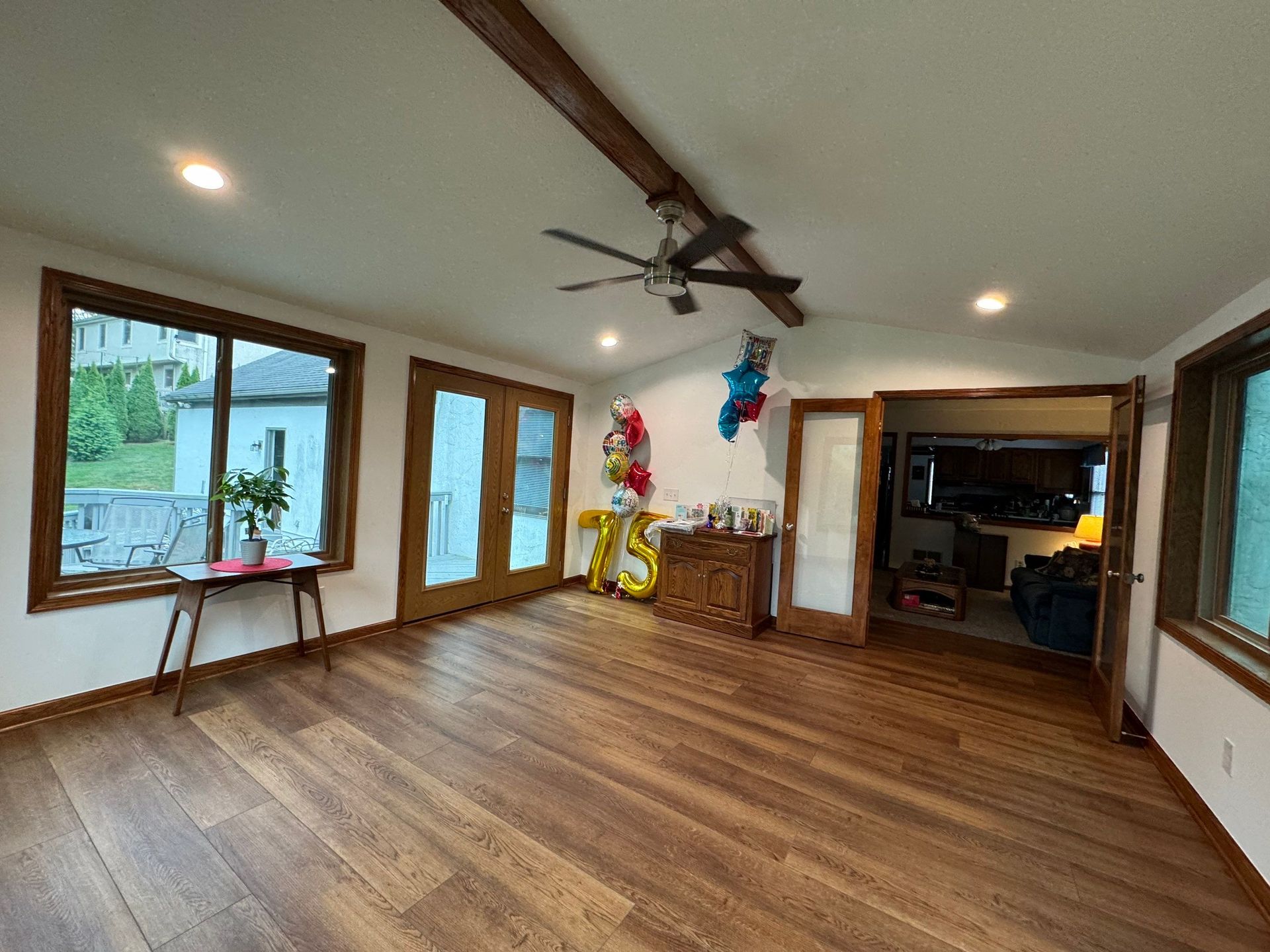 Empty hardwood-floored living room with ceiling fan, recessed lights, and large windows and doors