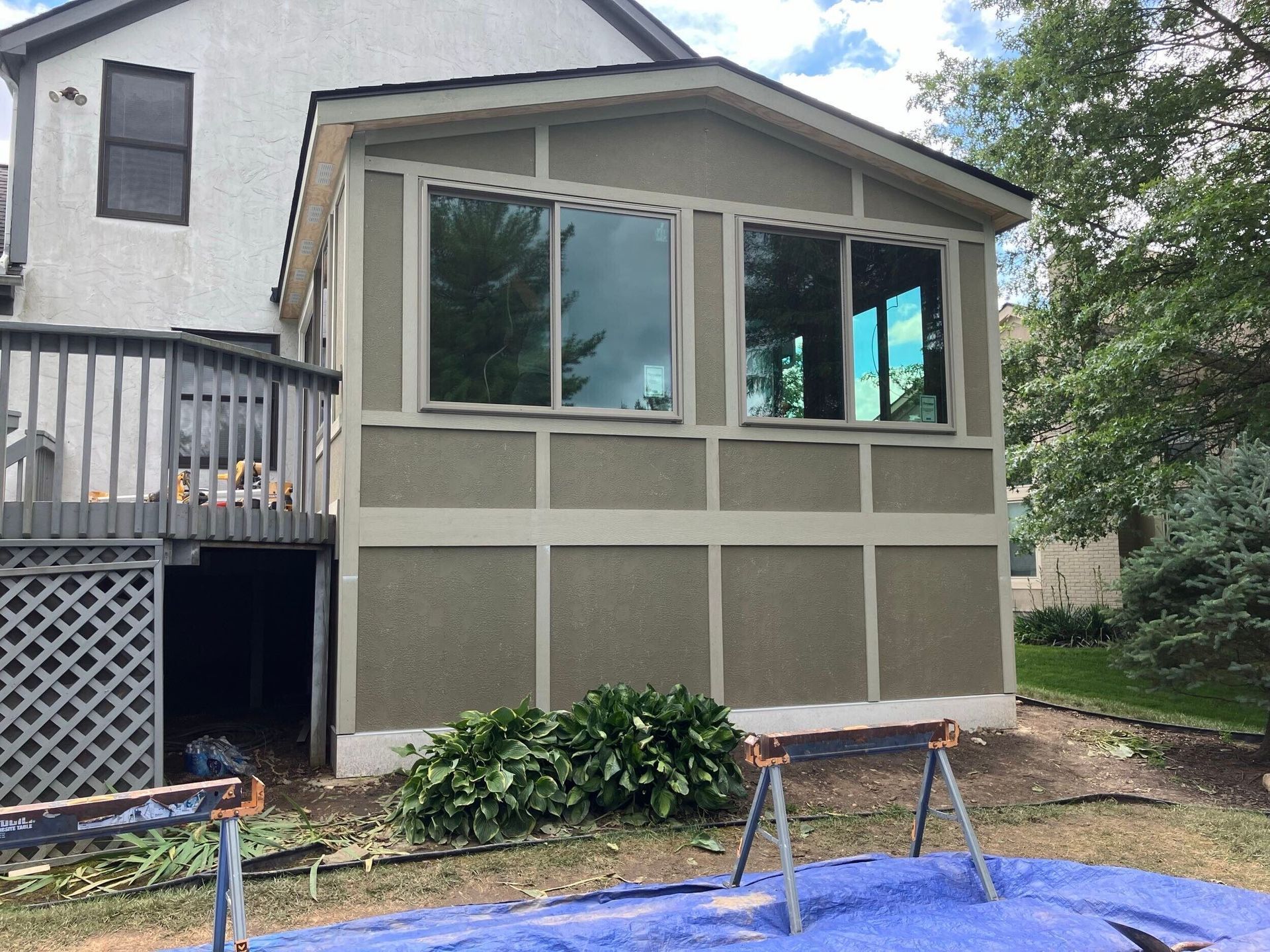 Side view of a house with a screened porch, beige siding, and a small garden bed below the windows.
