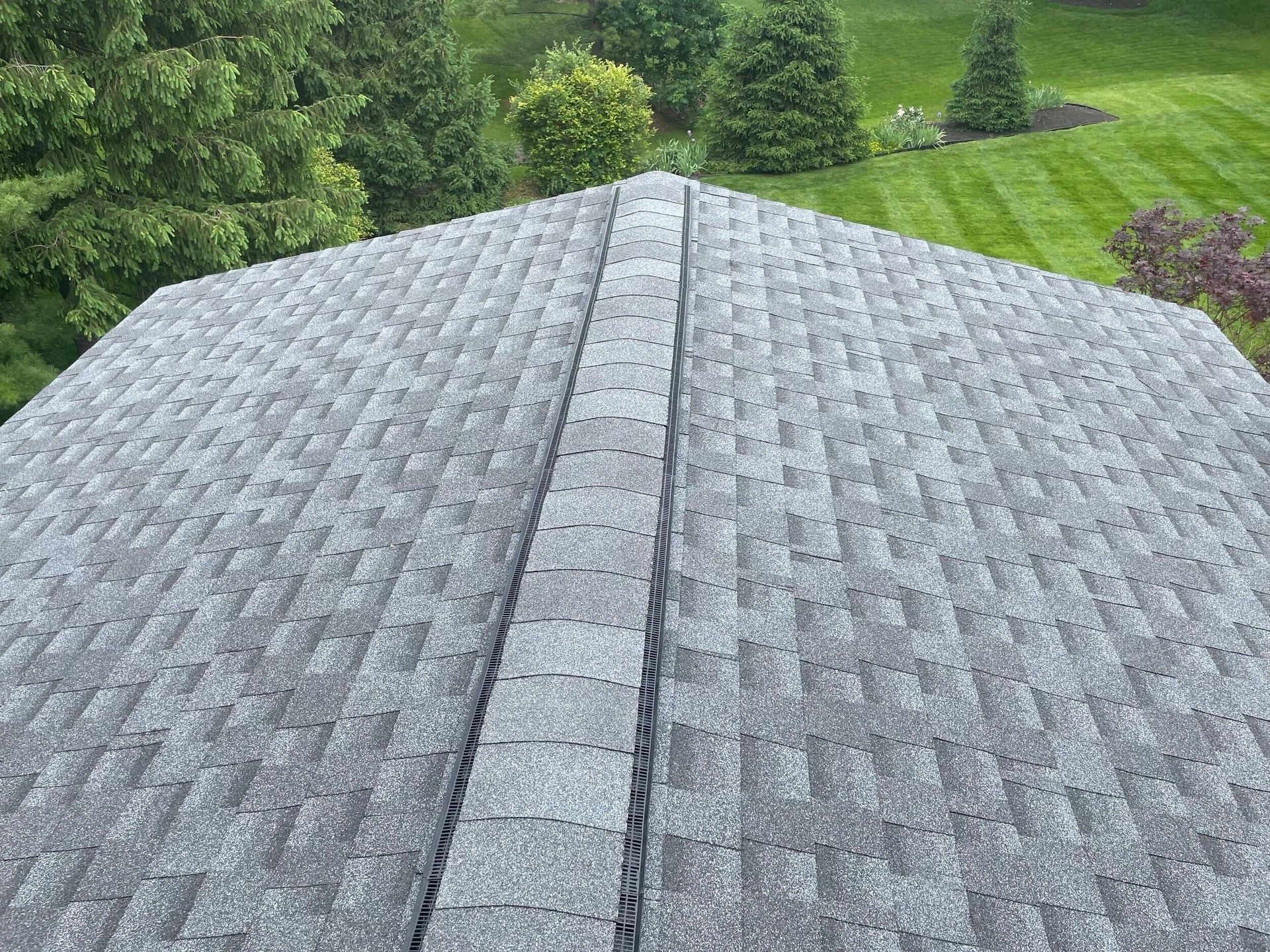 Gray shingled roof with a central ridge, overlooking green trees and lawn below