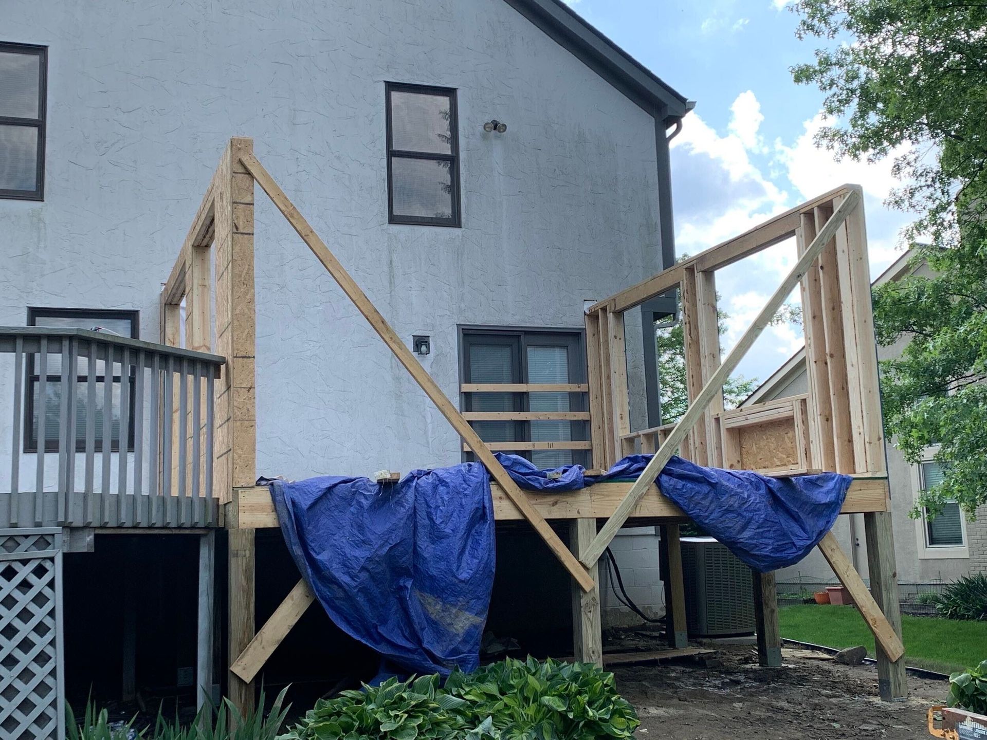 Partially built wooden deck framed with blue tarps beside a house