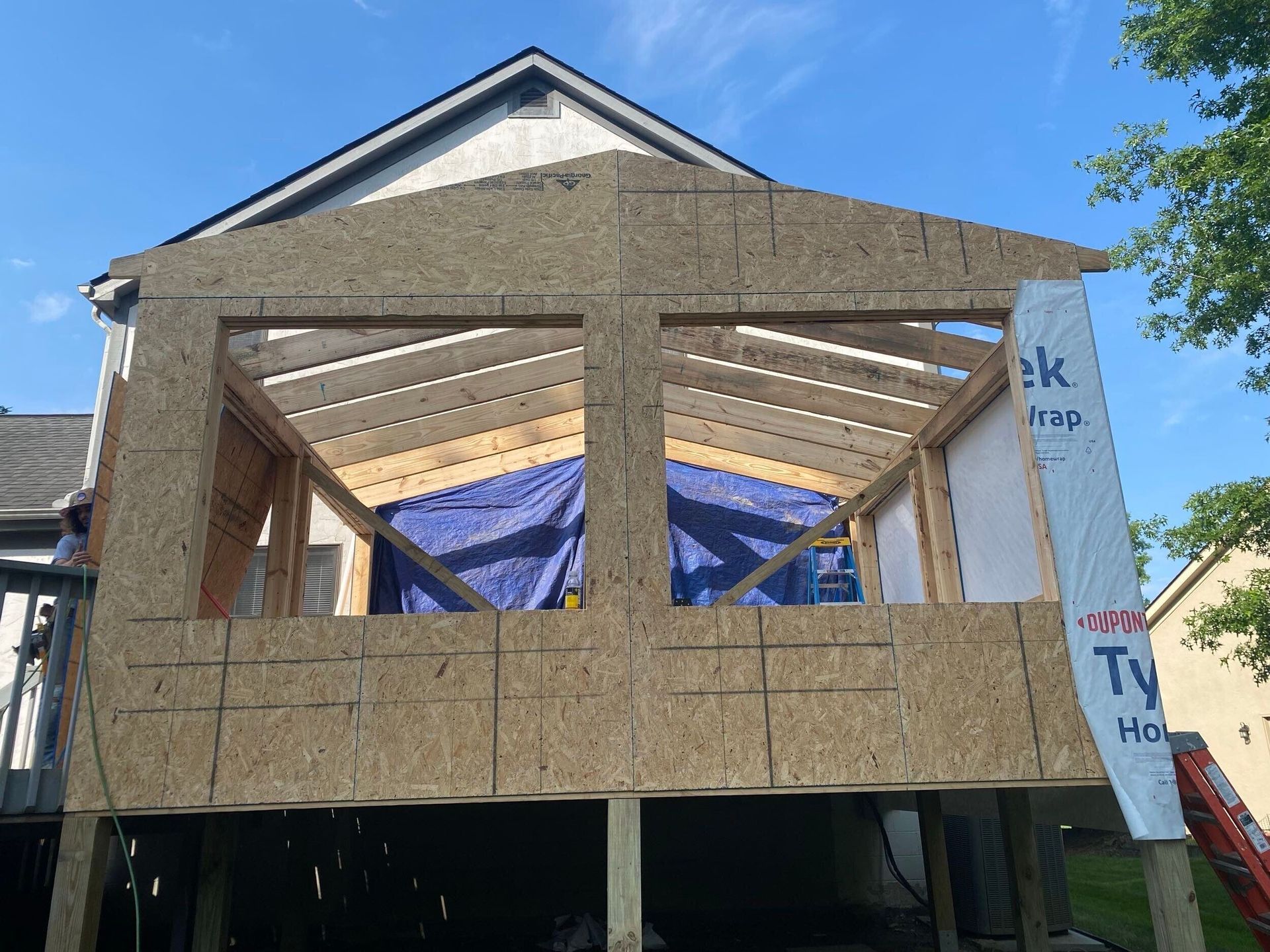 Partially framed house under construction with exposed plywood walls and roof trusses against a blue sky