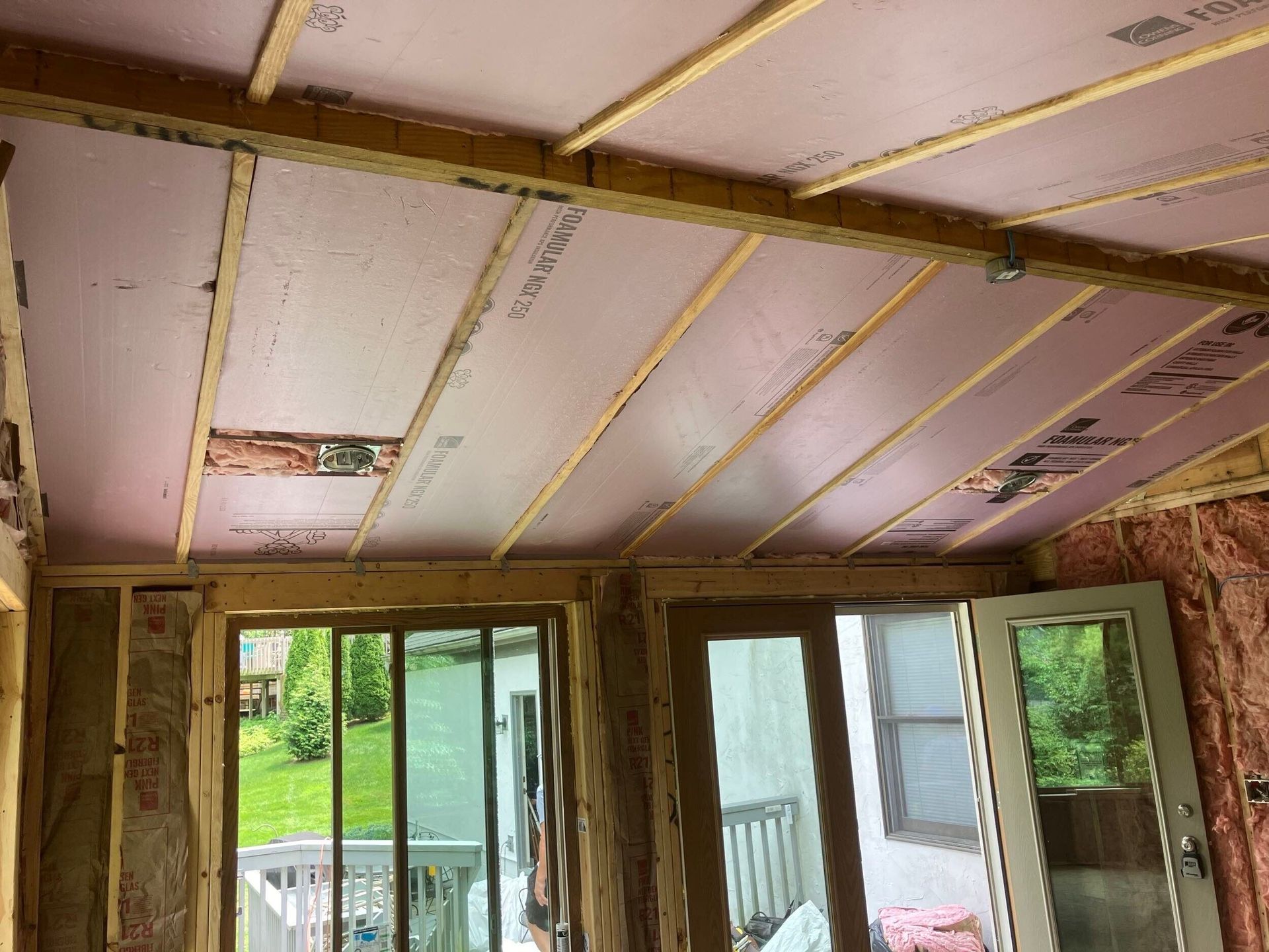 Partially finished room ceiling with exposed insulation strips and sliding glass doors to a porch outside
