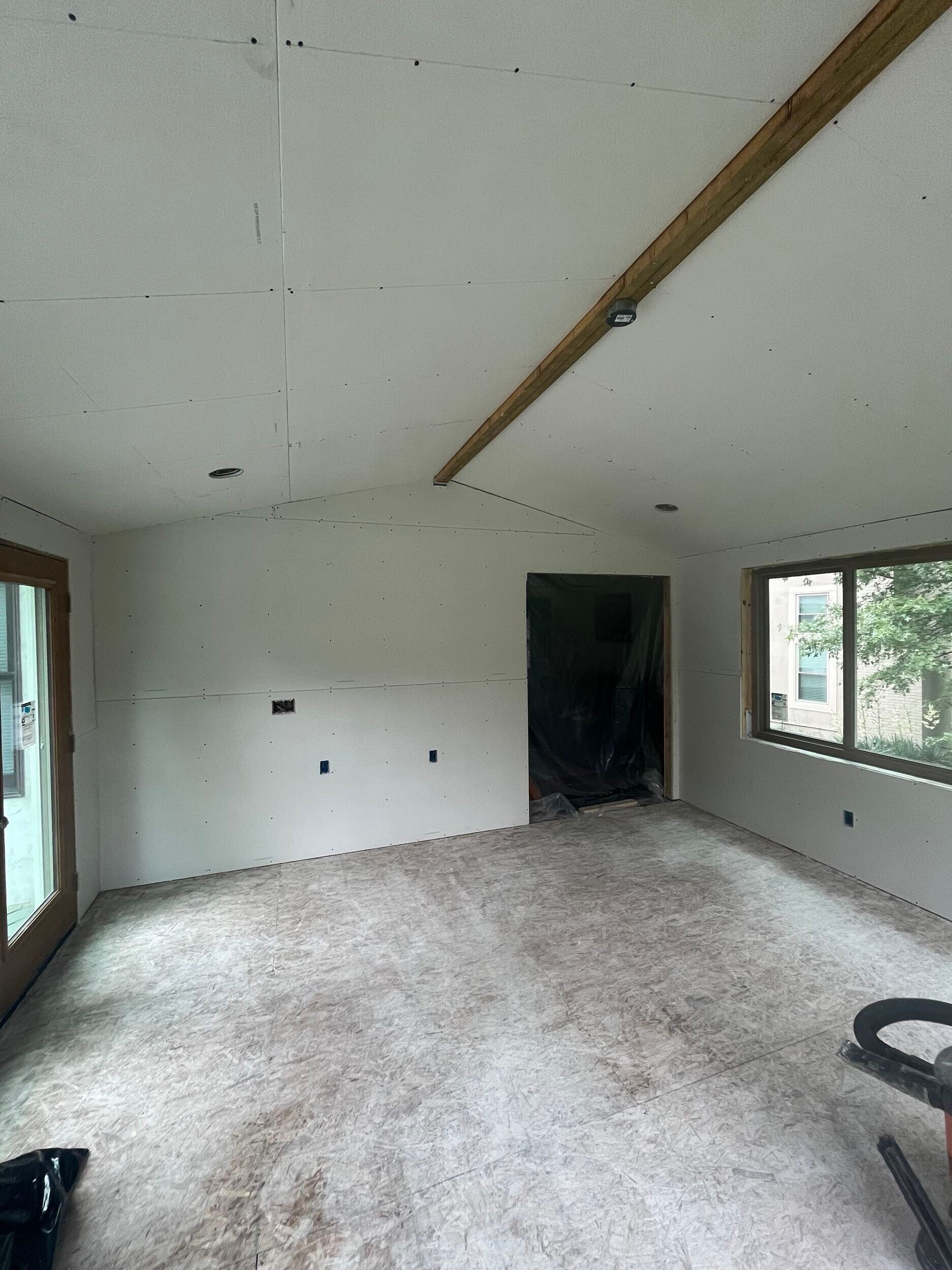 Empty unfinished room with white walls, sloped wood beam ceiling, carpeted floor, and windows on the right.
