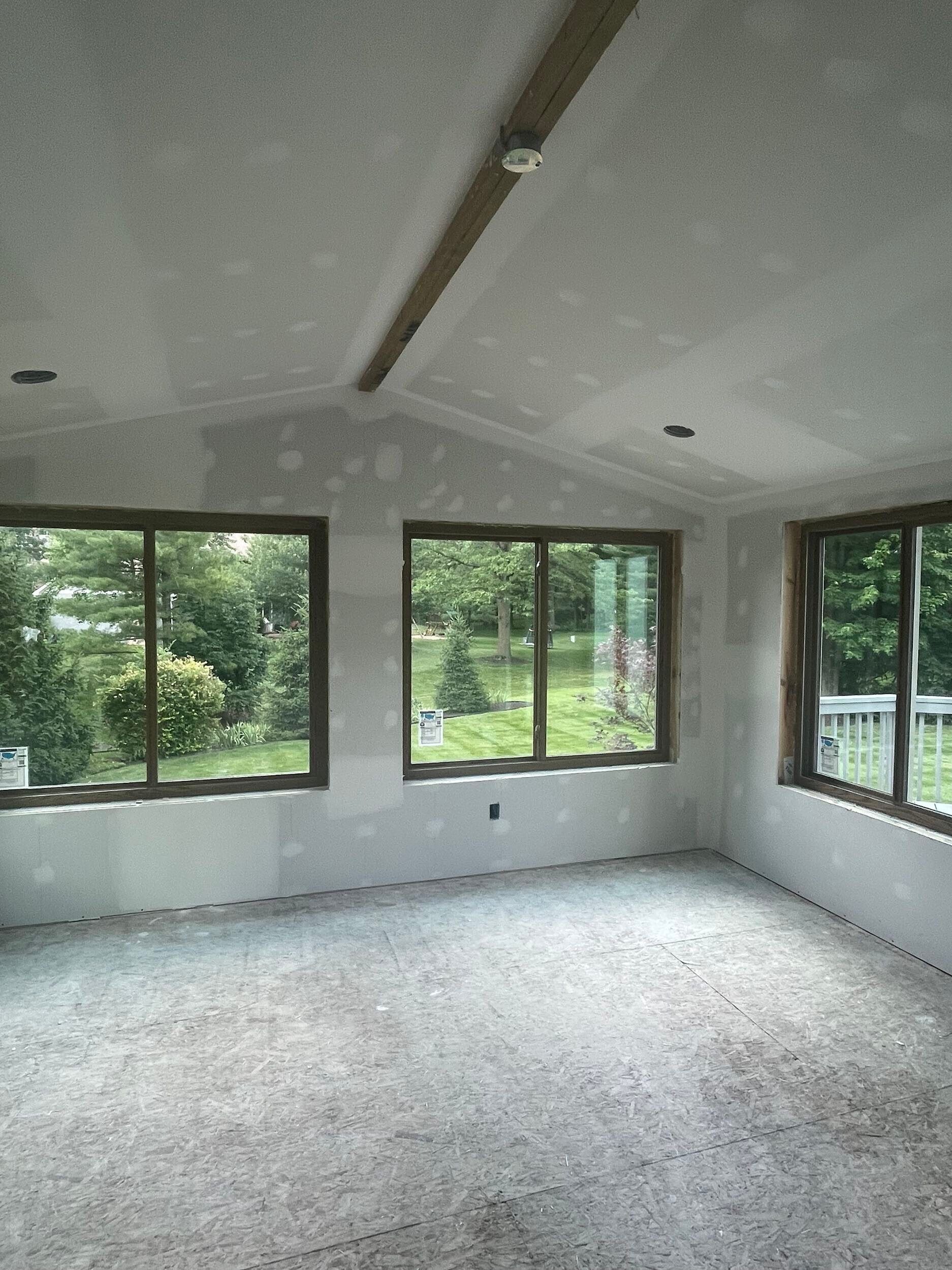 Empty carpeted room with large windows, white walls, and a vaulted ceiling.