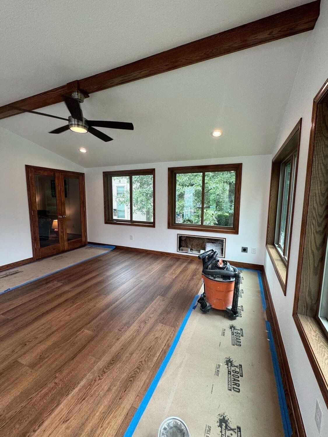 Empty room with wood floors, white walls, black ceiling fan, and three windows.