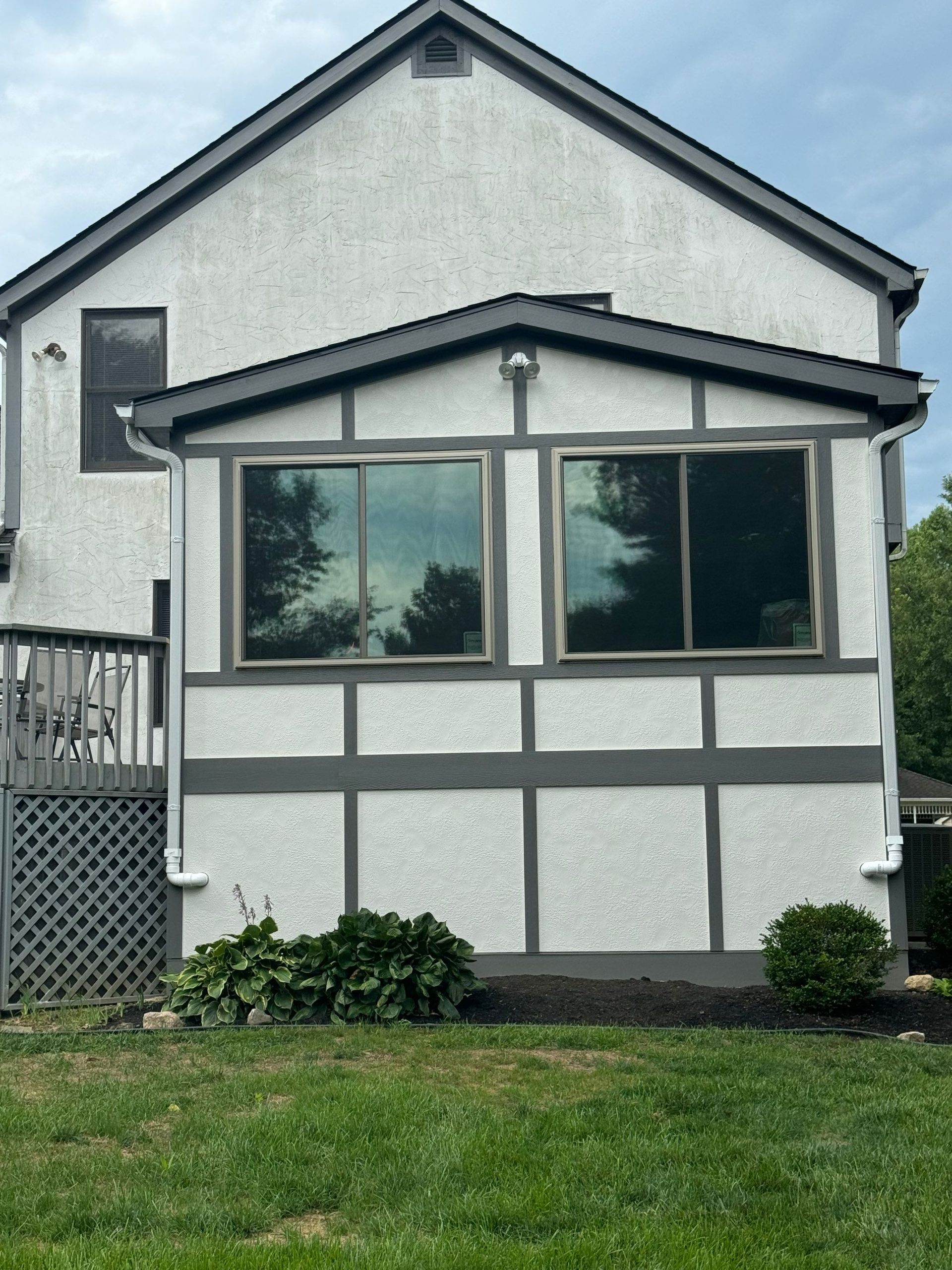 White two-story house exterior with gray trim, large front windows, and a small lawn