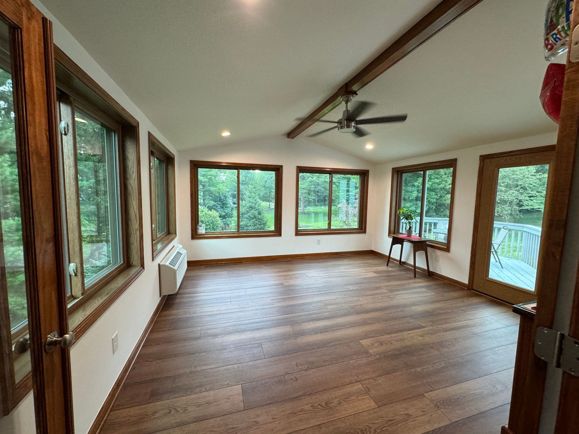 Empty sunroom with wood floors, large windows, ceiling fan, and white walls.