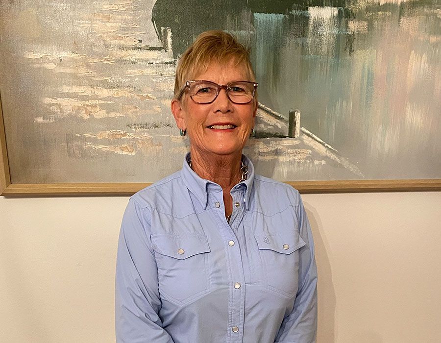 Smiling person in a light blue shirt standing indoors in front of an abstract painting.
