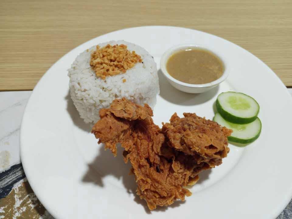 A serving of crispy fried chicken with garlic rice topped with fried garlic, brown gravy, and two cucumber slices.