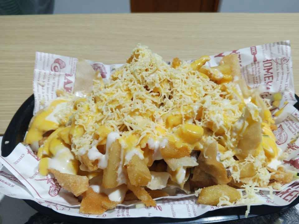 A basket of crispy French fries topped with yellow cheese sauce, white sauce, and shredded cheese on printed paper.