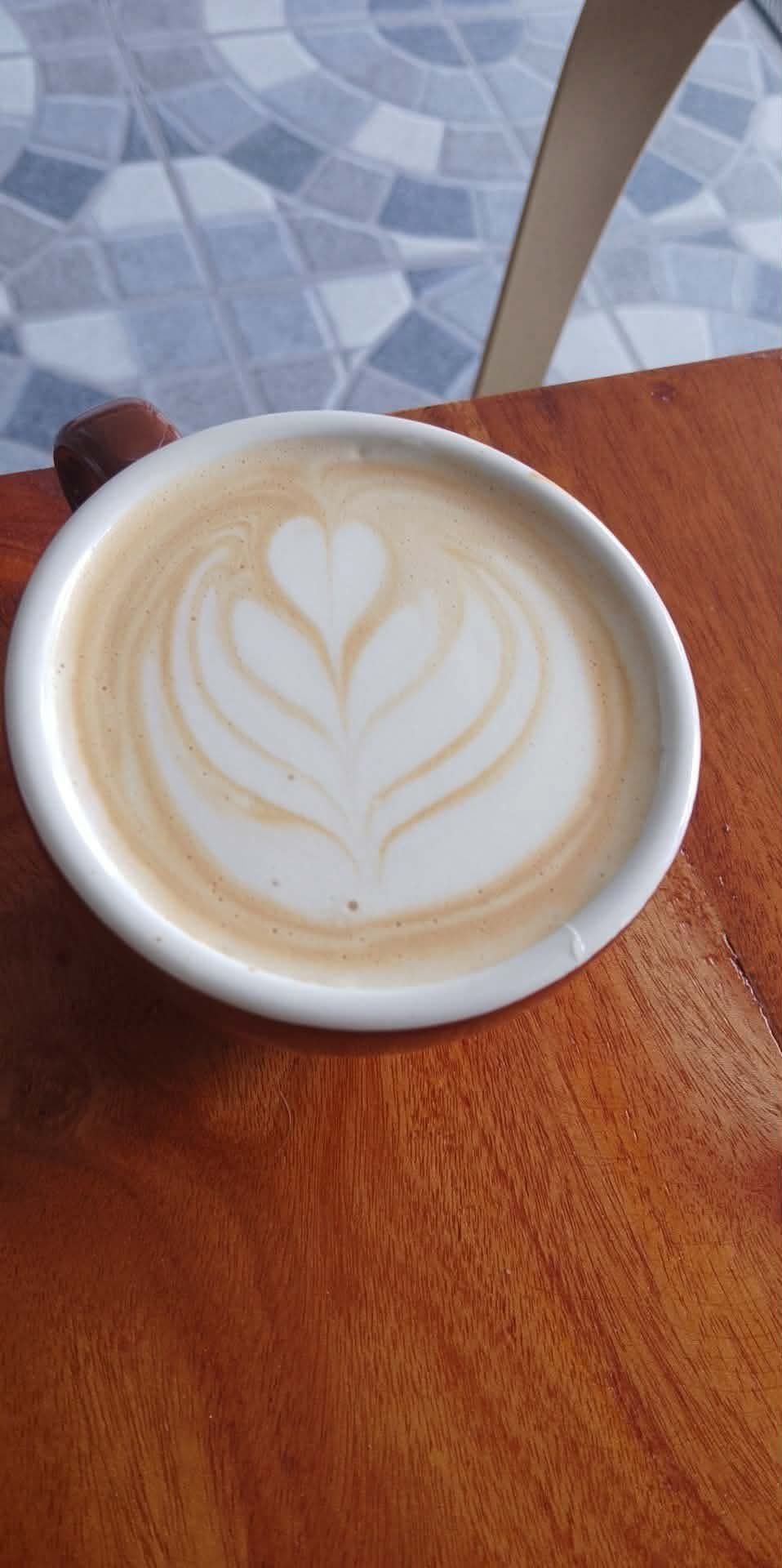 A cup of coffee on a wooden table, featuring intricate rosetta latte art on its foam surface.
