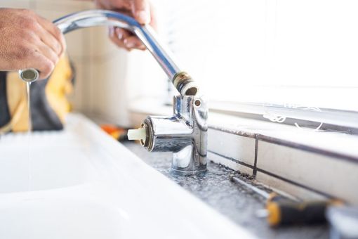 Hands rinsing a chrome kitchen faucet in a white sink