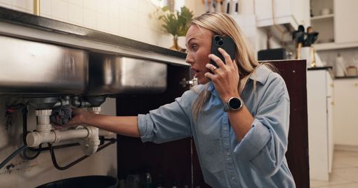Person on phone inspecting machinery under a stainless-steel kitchen counter