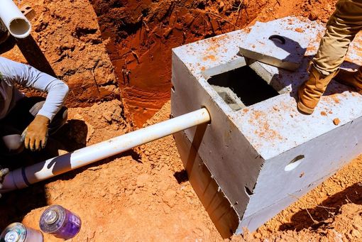 Workers installing a white pipe into a concrete utility box on red dirt soil