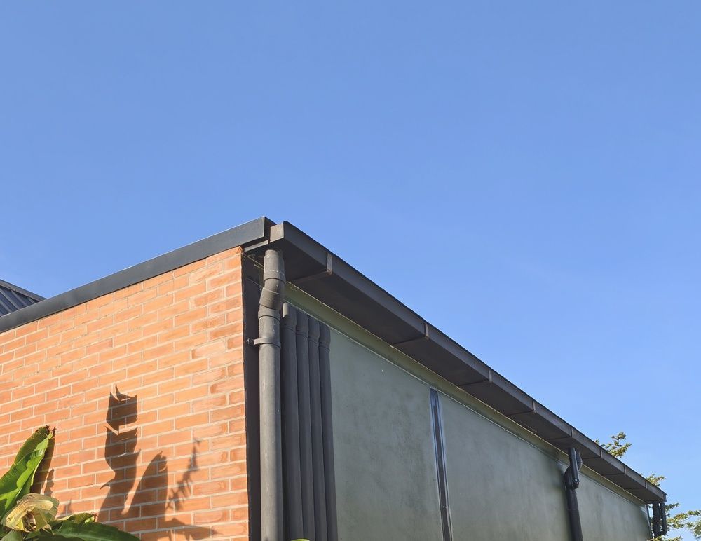 Brick and stucco building corner under a clear blue sky, with a gutter and roof edge visible