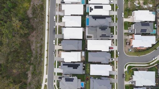 Aerial view of suburban homes with white and gray roofs along a curved street and trees.