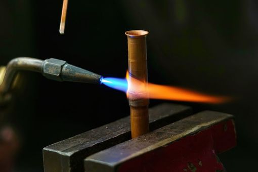 Torch flame heating a brass tube held in a vise on a workshop bench