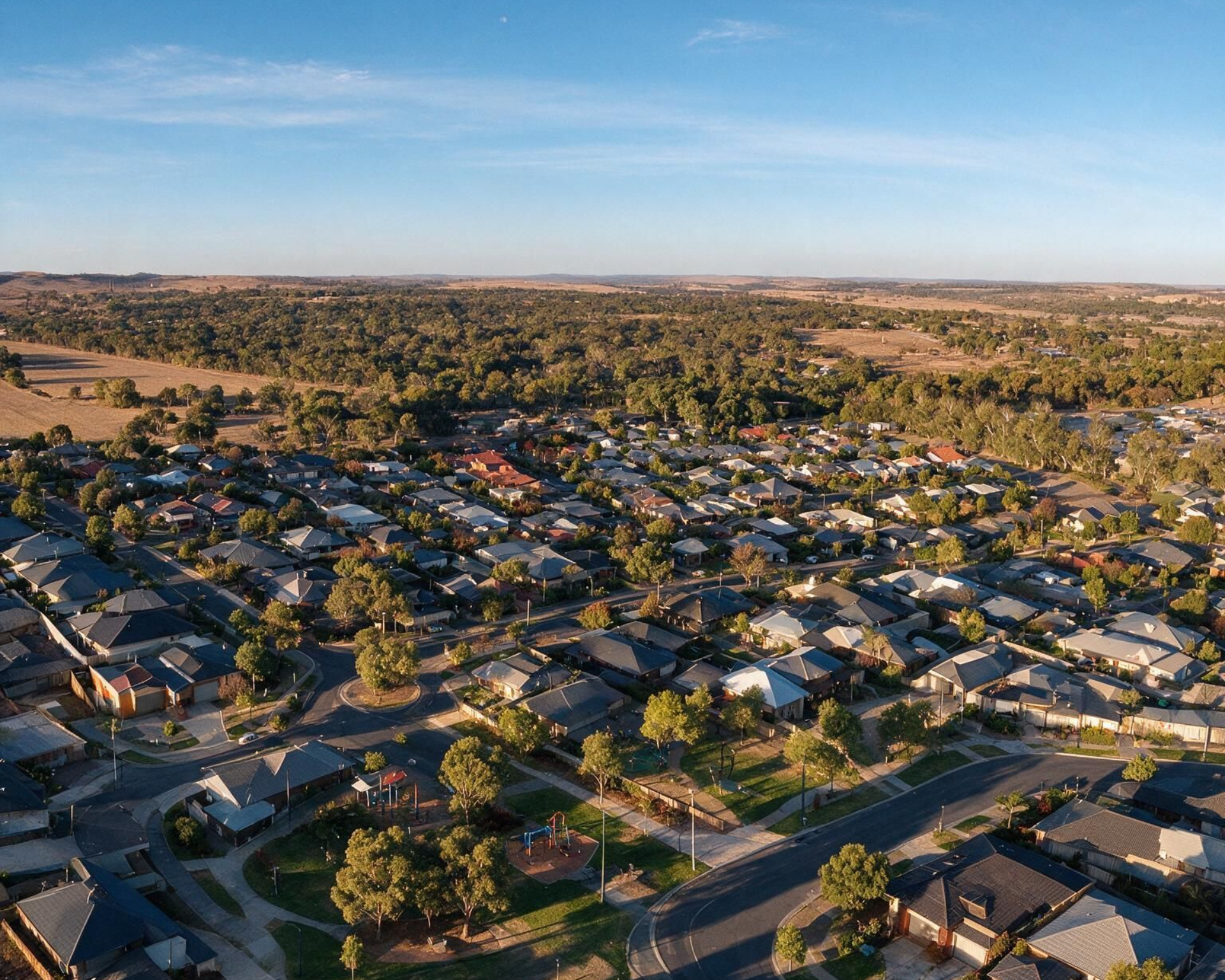 Aerial view of a suburban neighborhood with houses, streets, and trees in warm late-day light