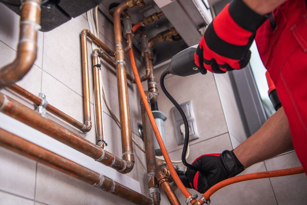 Plumber in red gloves repairing copper pipes under a sink with a wrench.